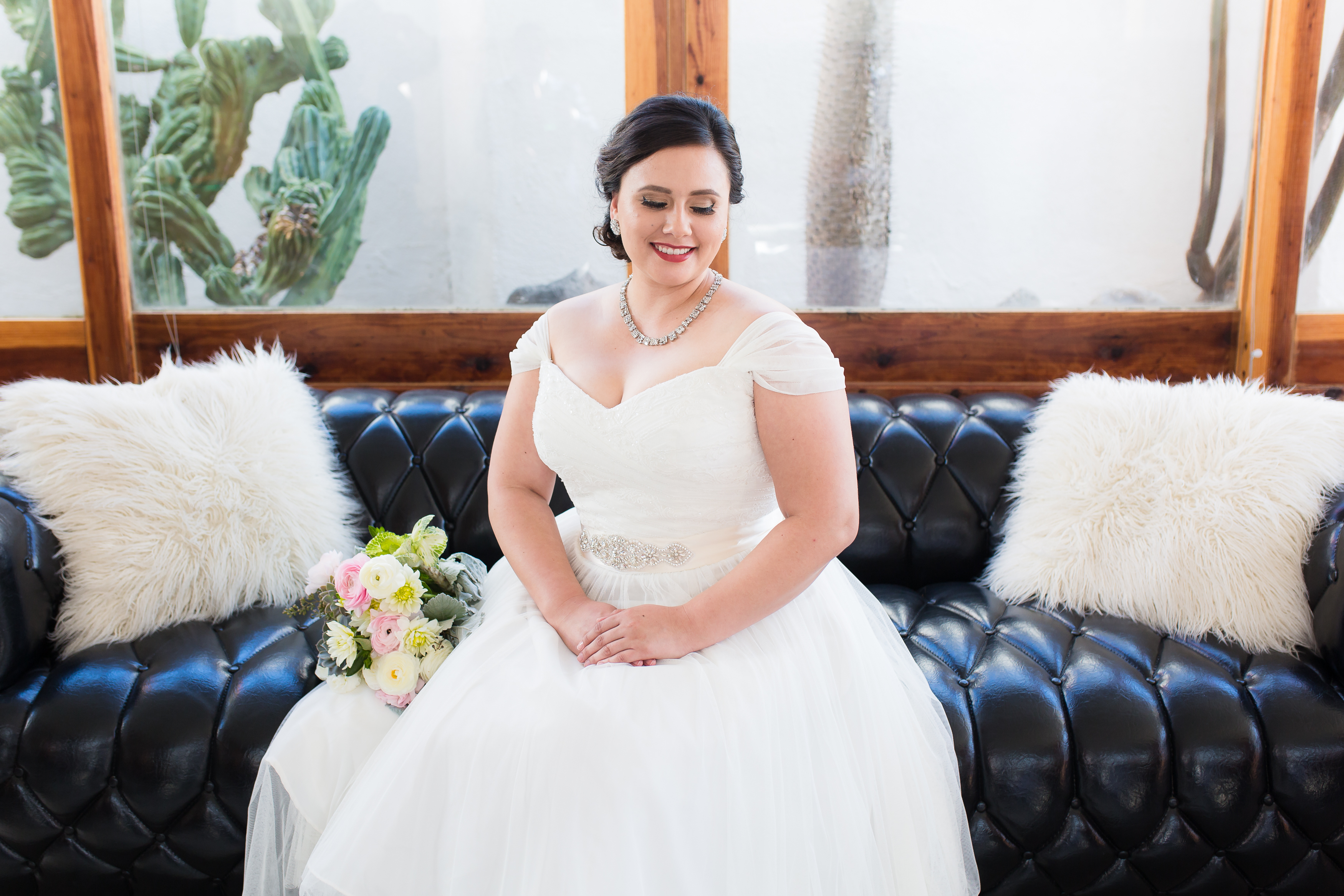 Bride sitting on leather couch in wedding dress looking over shoulder