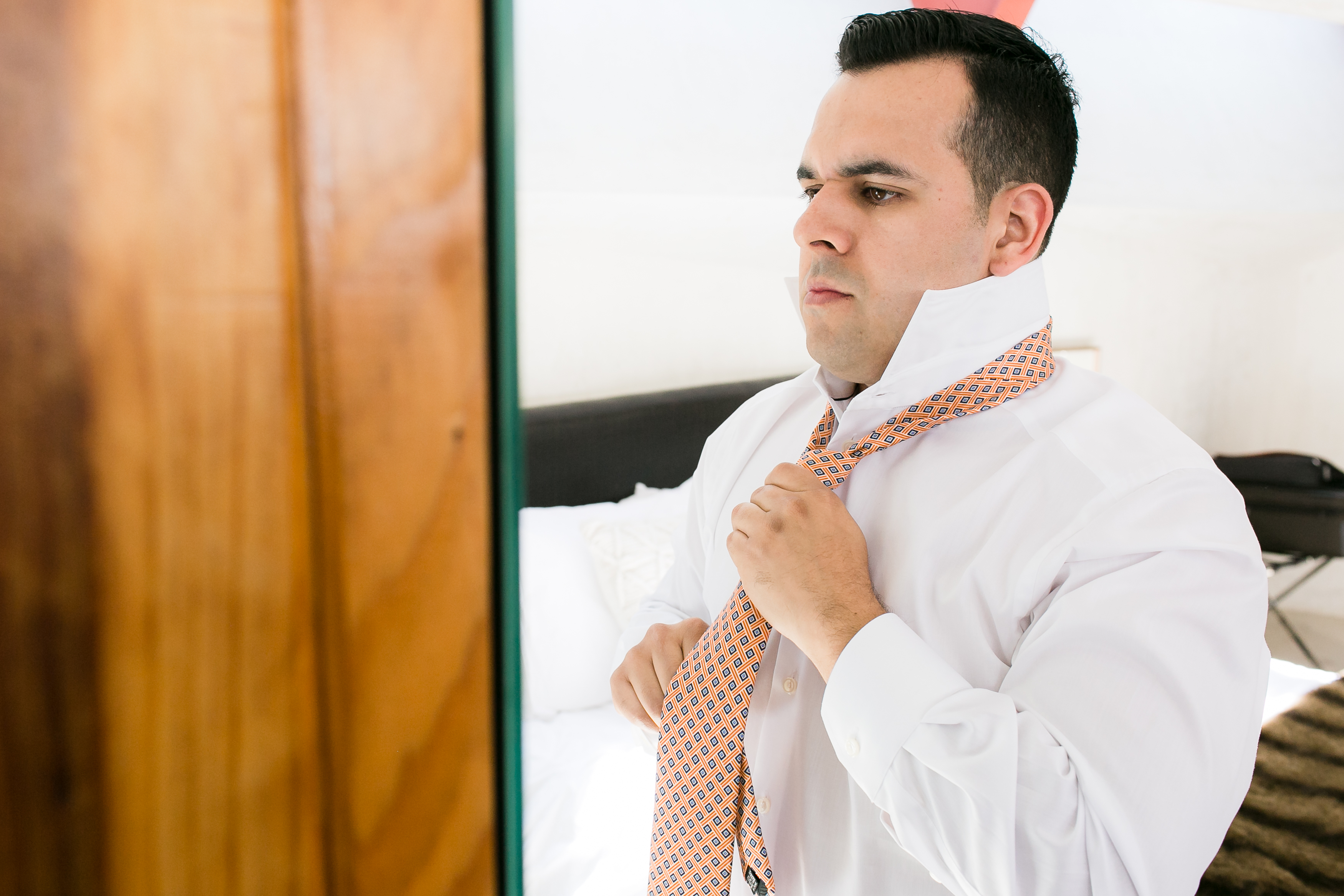 Man adjusting peach colored tie in mirror in hotel room