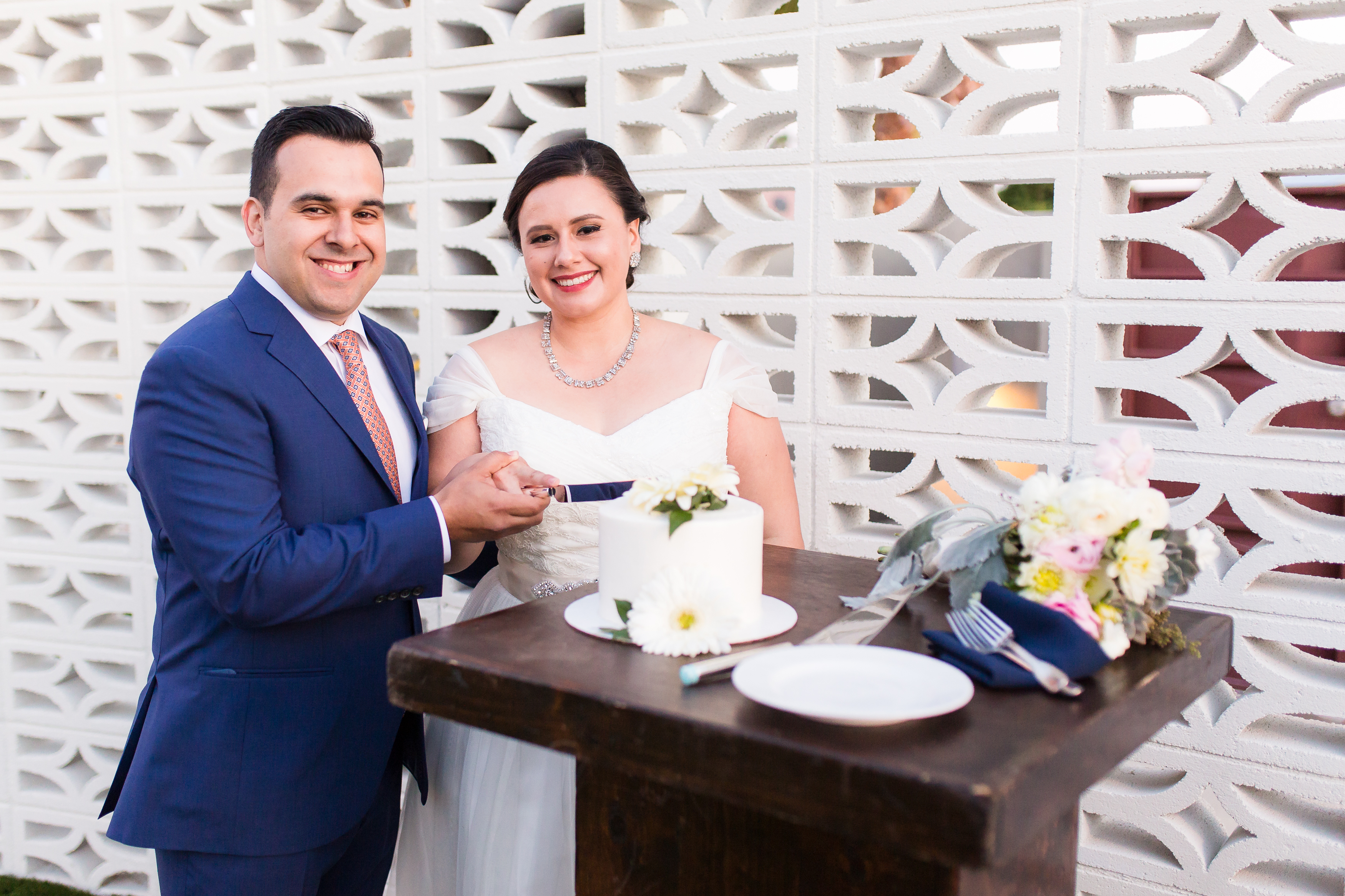Bride and groom cut small white wedding cake during outdoor reception