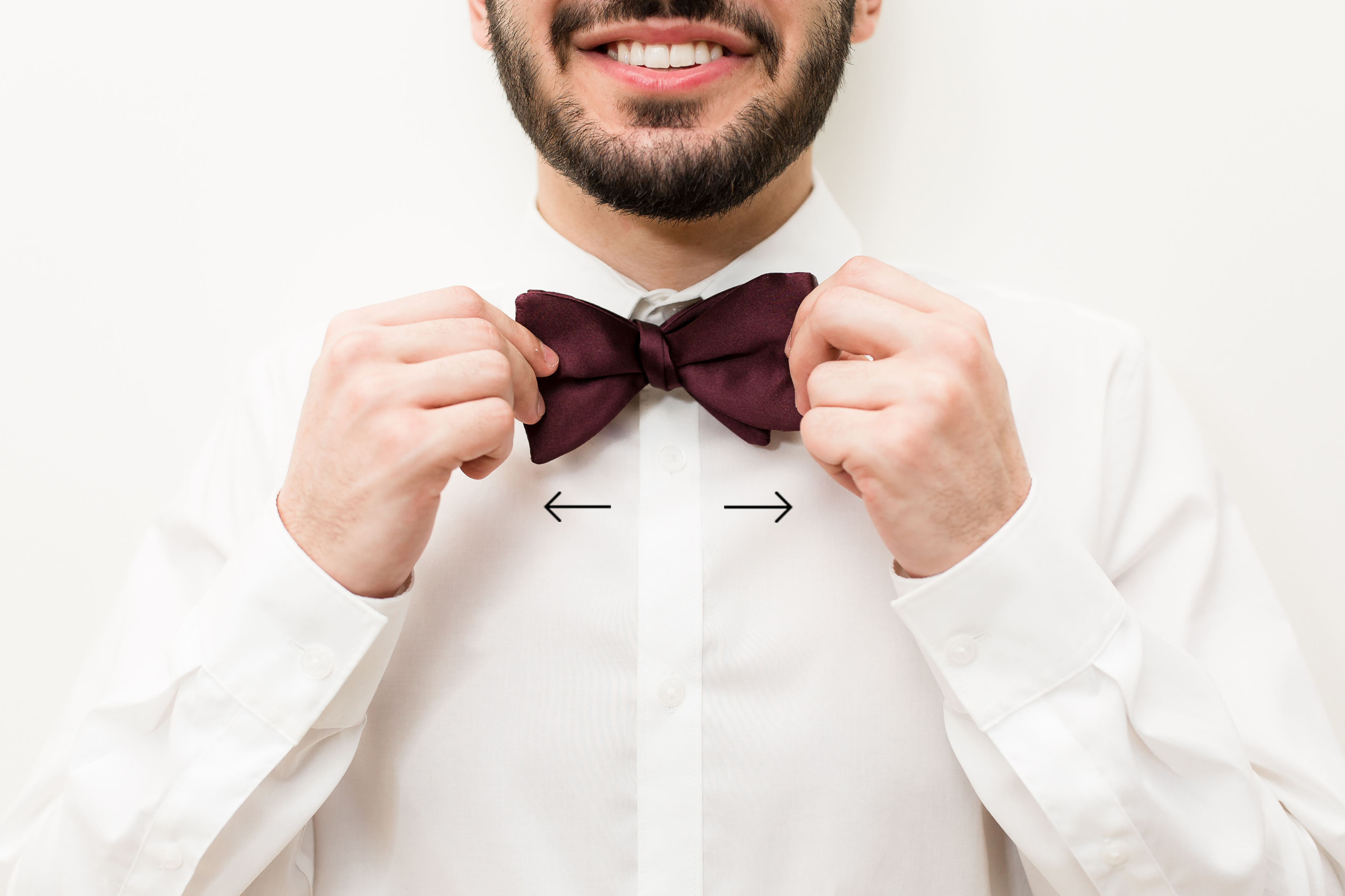 Groom smiling while adjusting burgundy bow tie