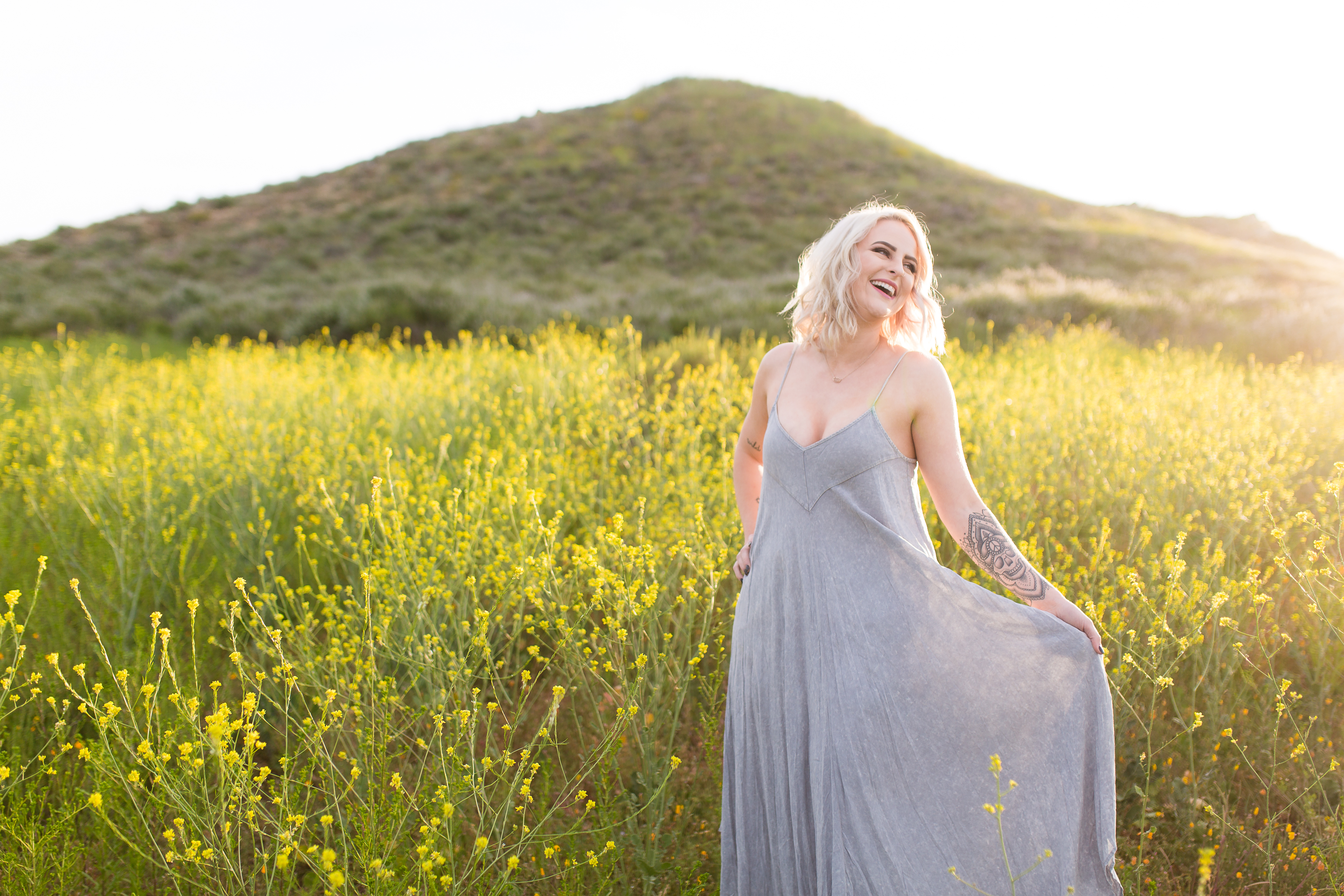 Blonde woman laughing in field of poppies by green hill at sunrise