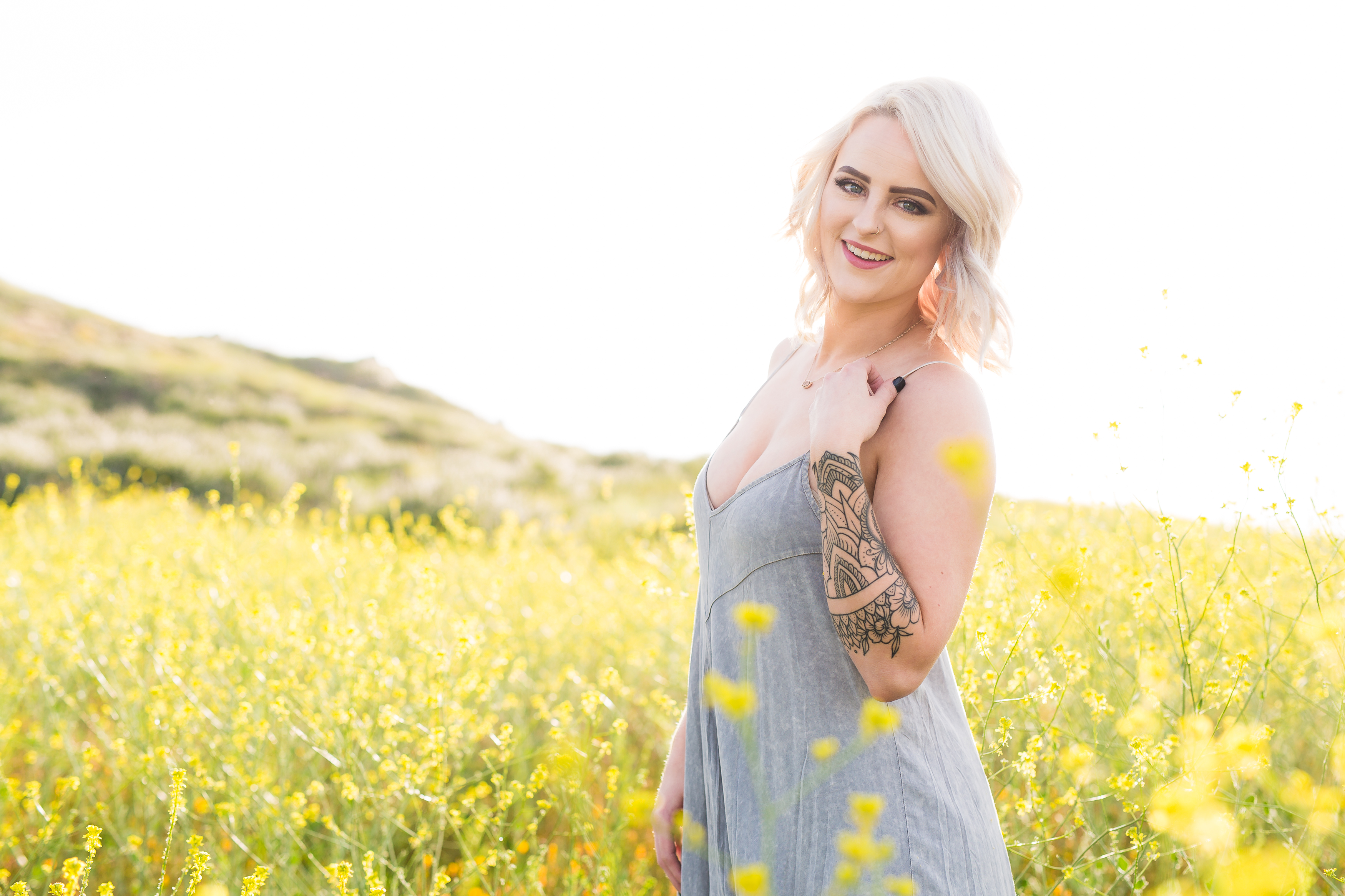Blonde model standing holding dress strap amidst yellow flowers