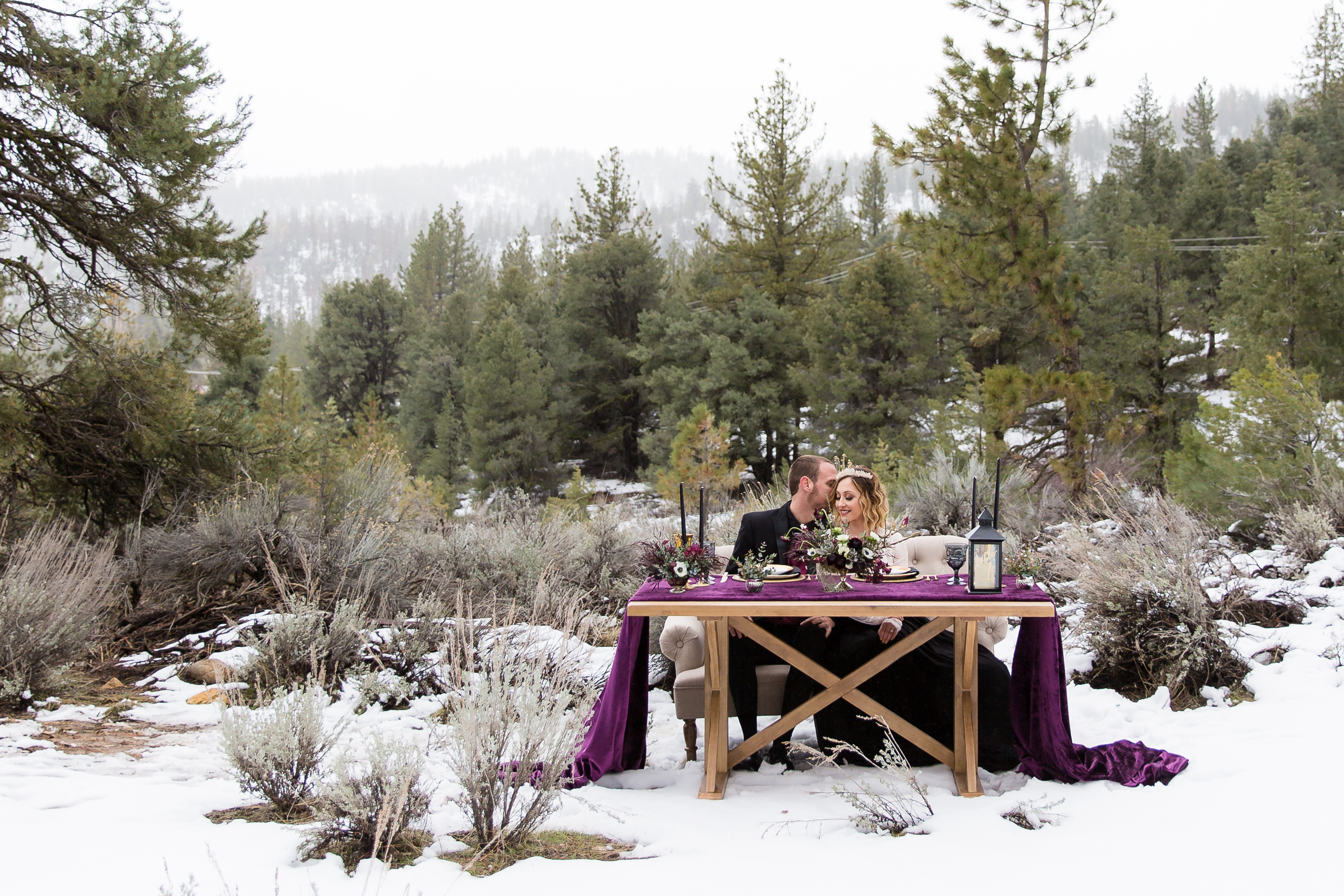 Groom whispering into fiancé's ear at sweetheart table in snow in CA