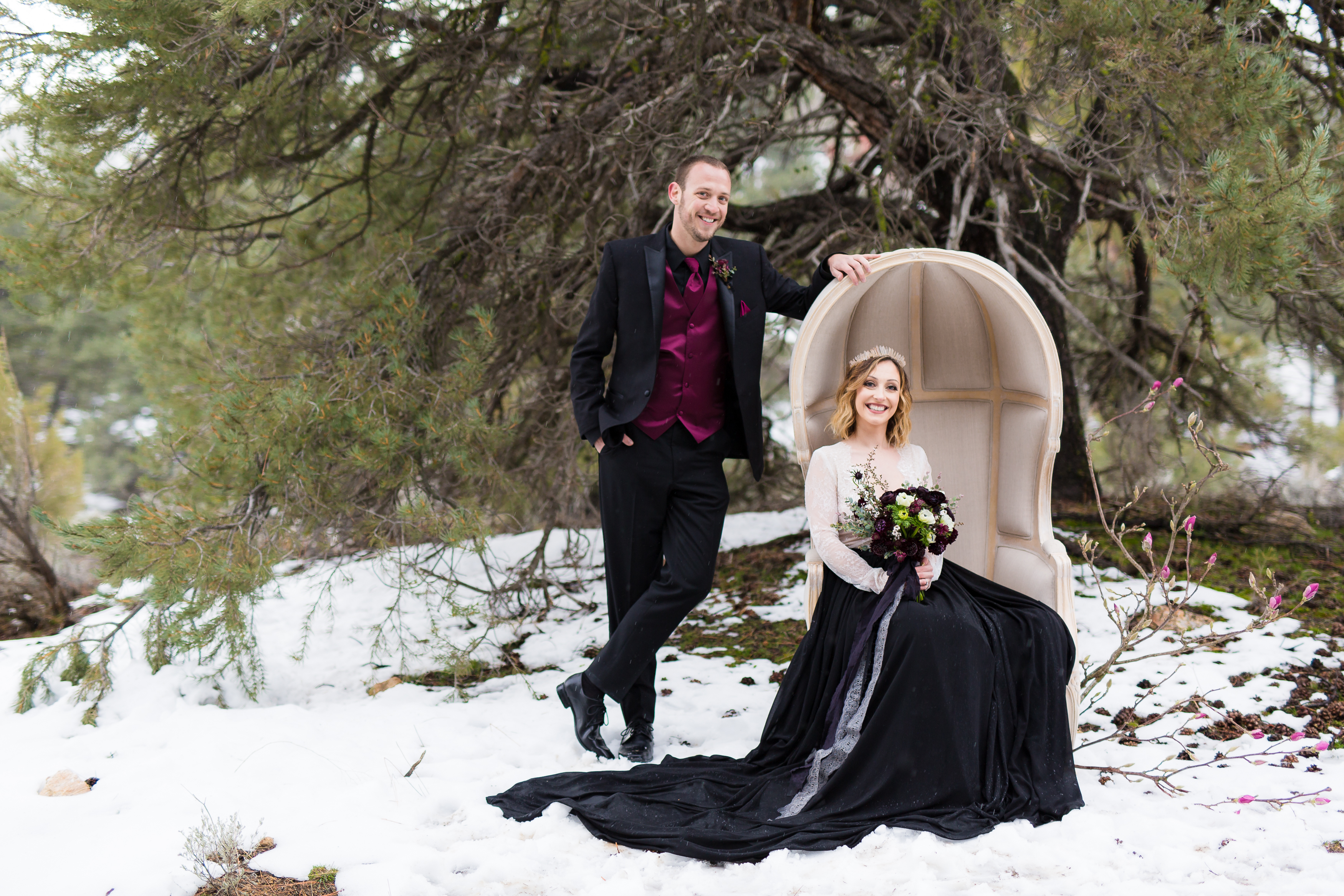 Husband leaning against chair while bride sits in snowy winterland