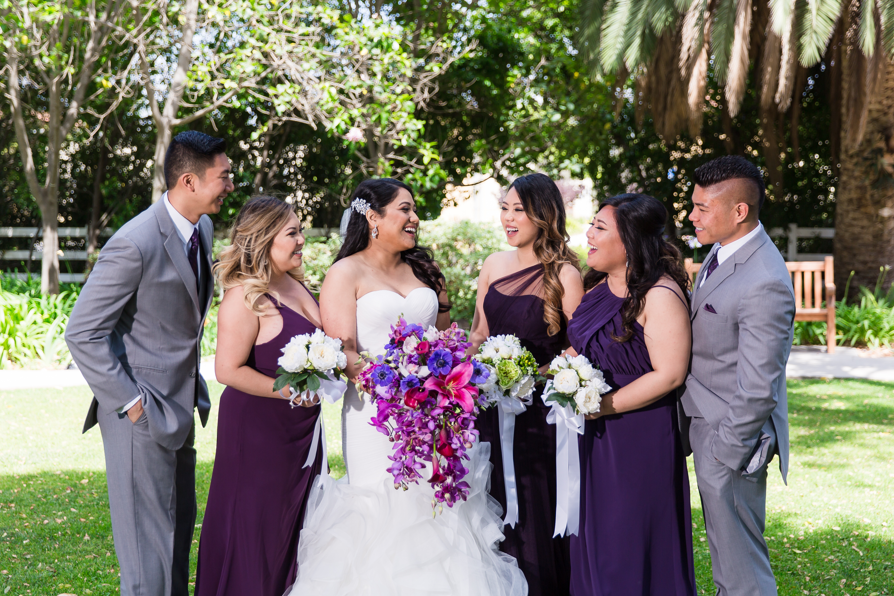 Wedding party laughing in towards each other surrounded by trees