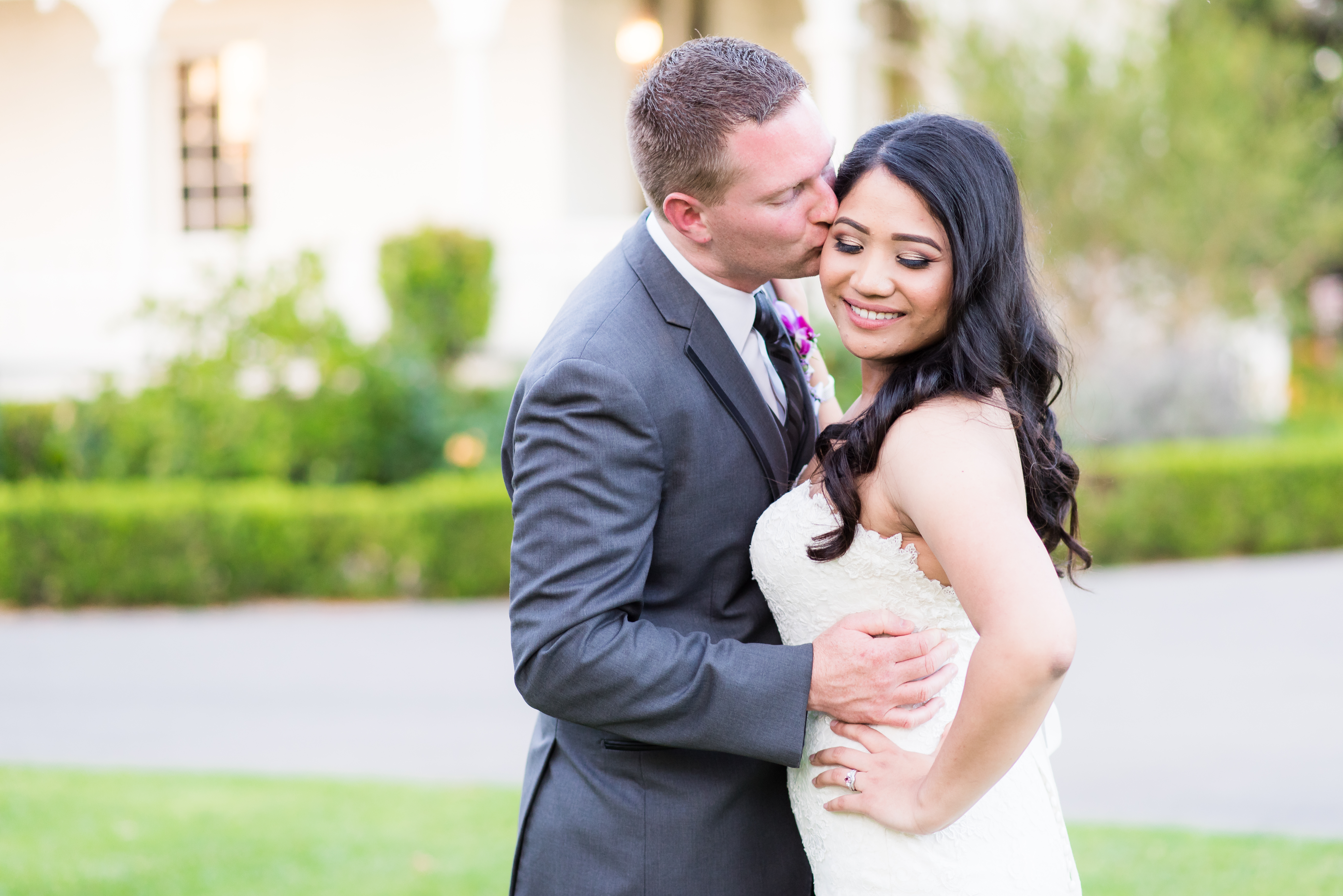Groom kisses bride on cheek while smiling over shoulder