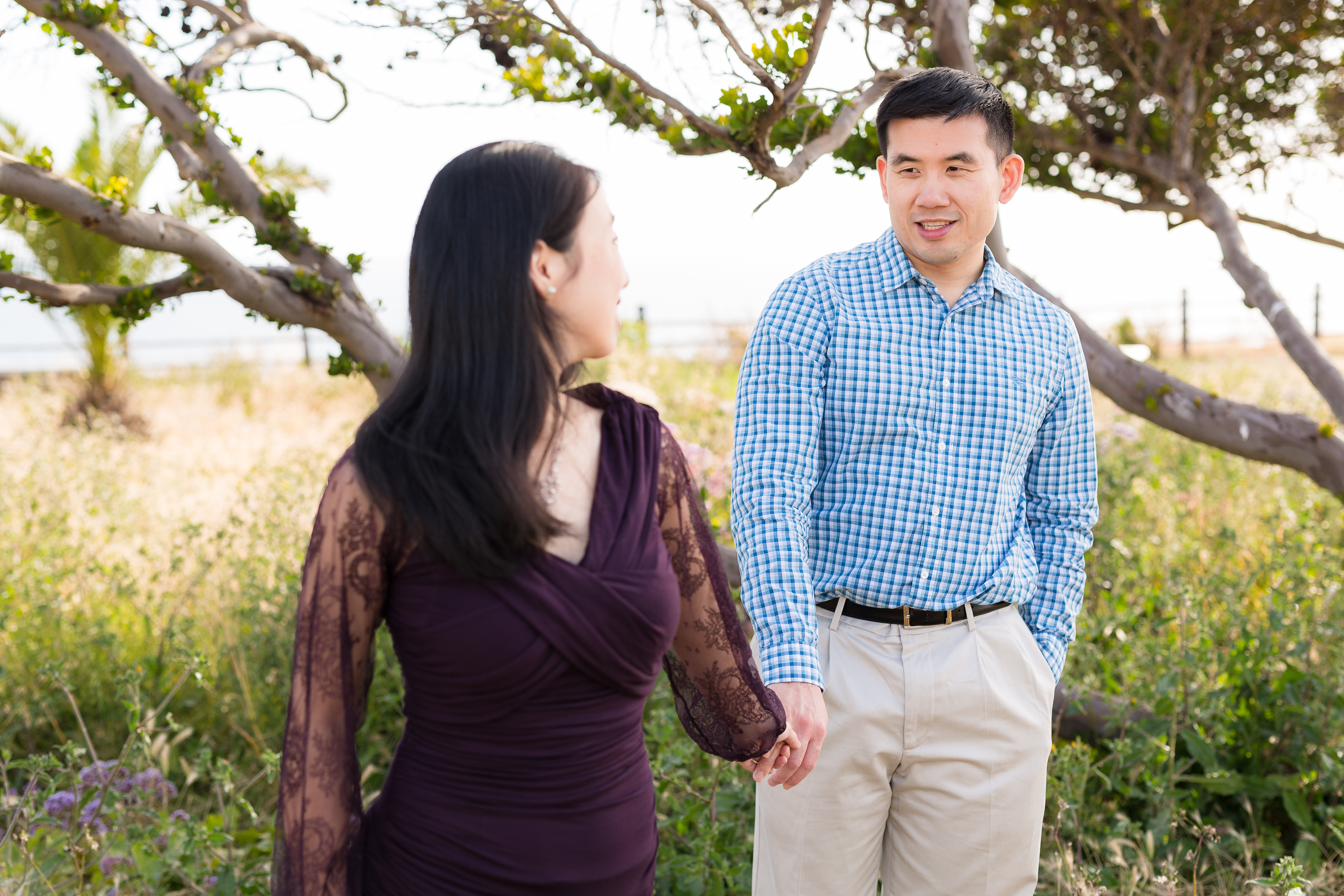 Asian man holding woman's hand in grass field at Point Vicente Lighthouse