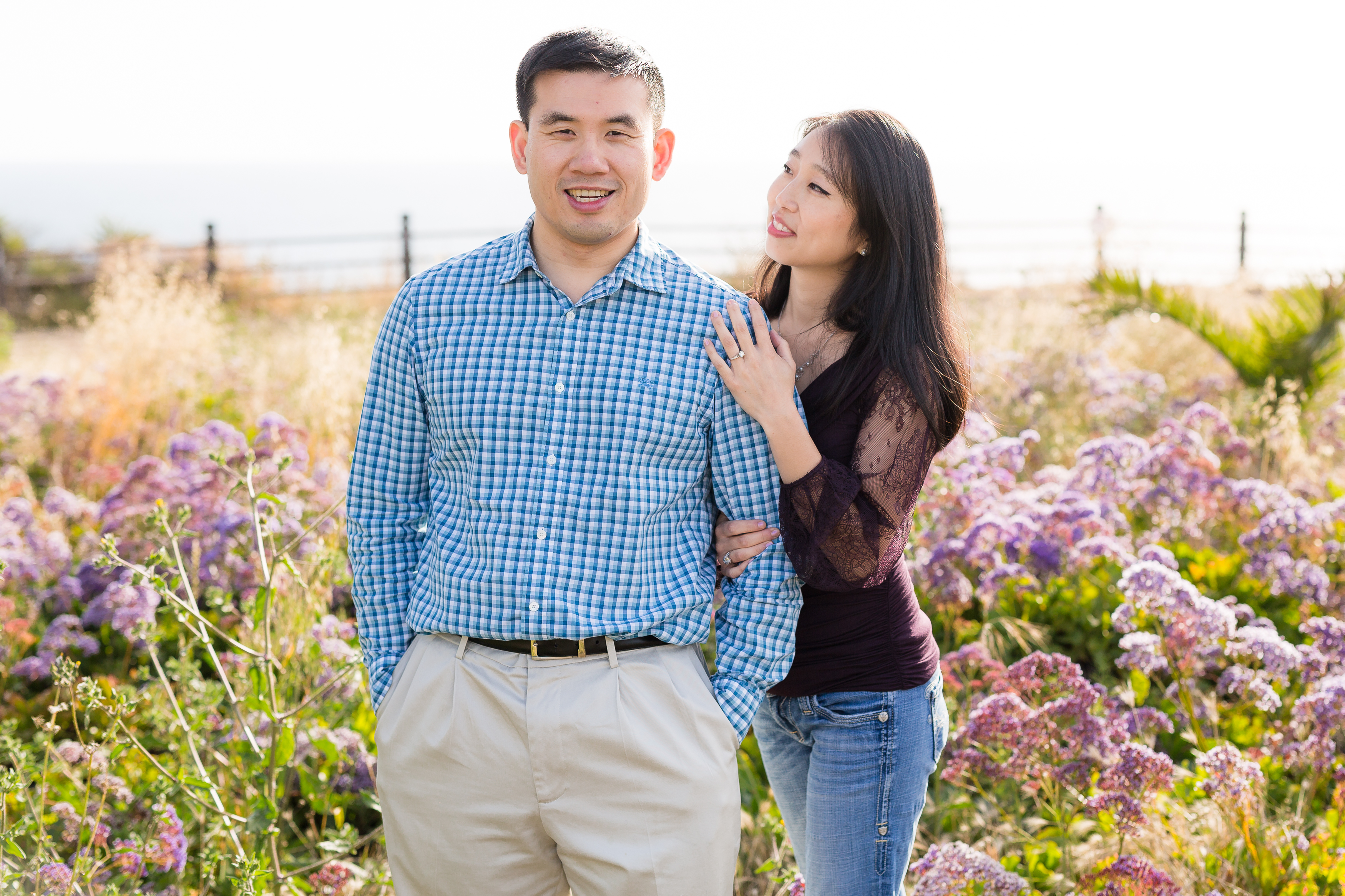 Man and woman standing in field of purple flowers by the ocean