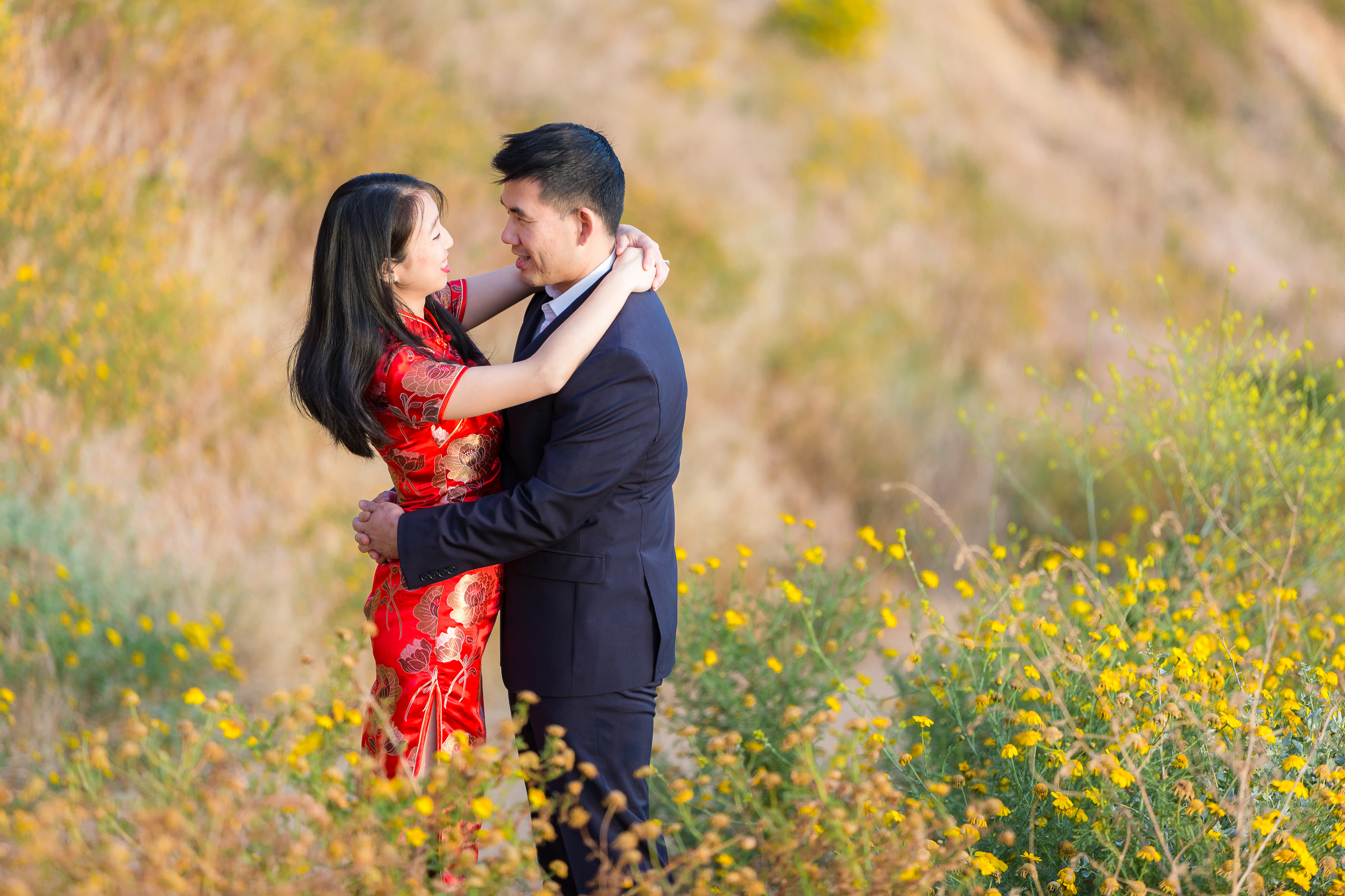 Engaged couple in traditional Chinese dress hugging in field of yellow flowers