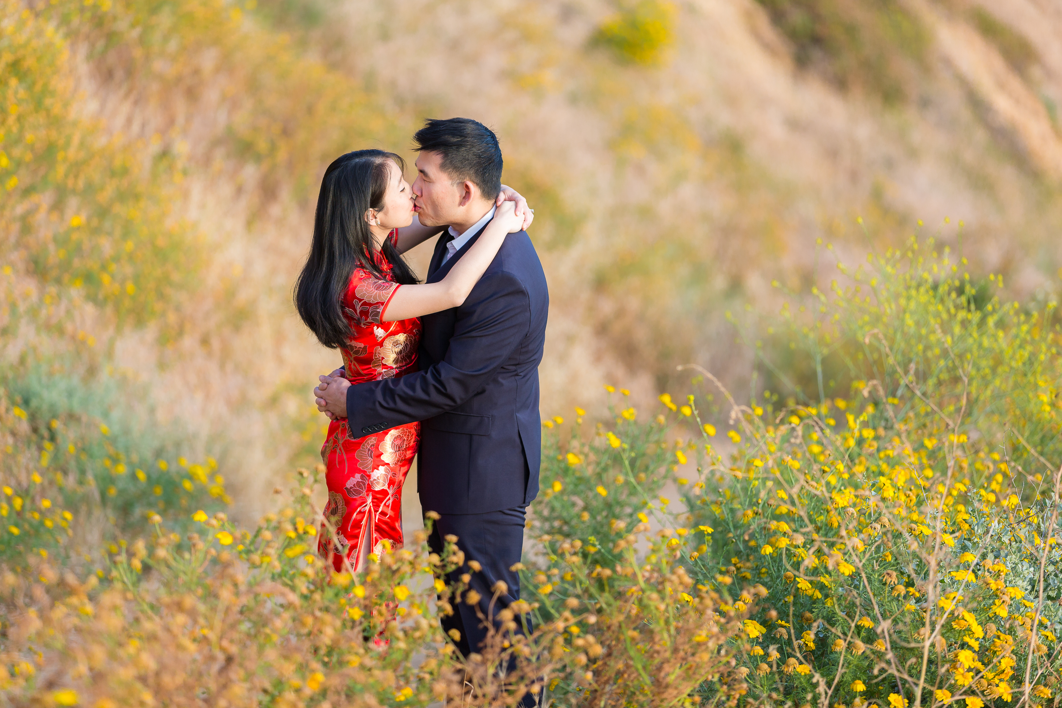 Engaged man and woman kissing amidst yellow flowers
