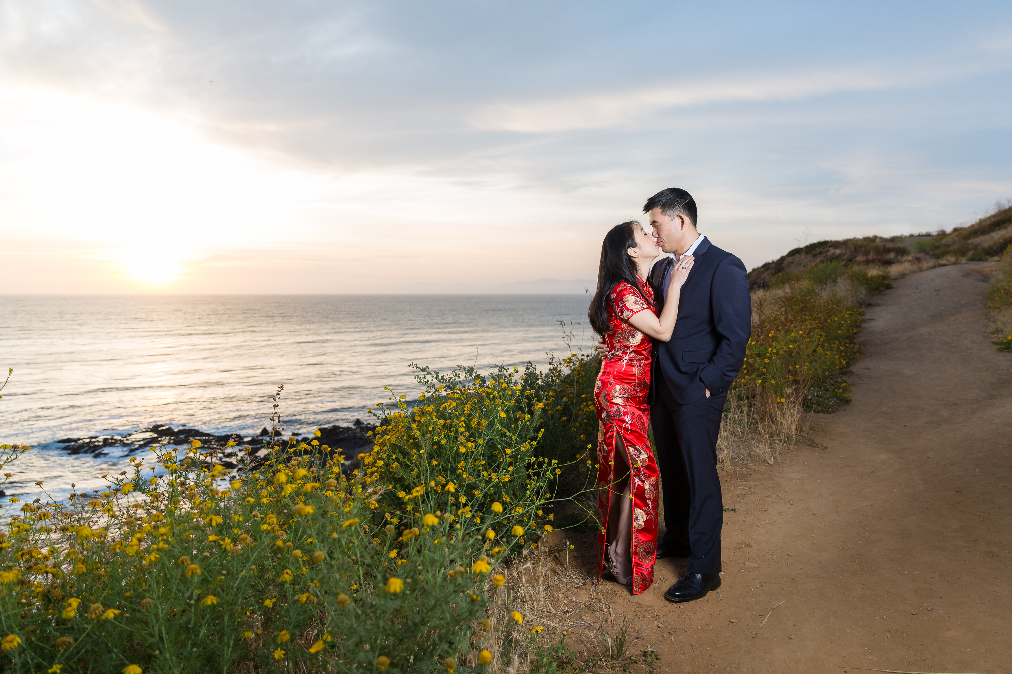 Engaged couple kissing along cliffside at sunset in California