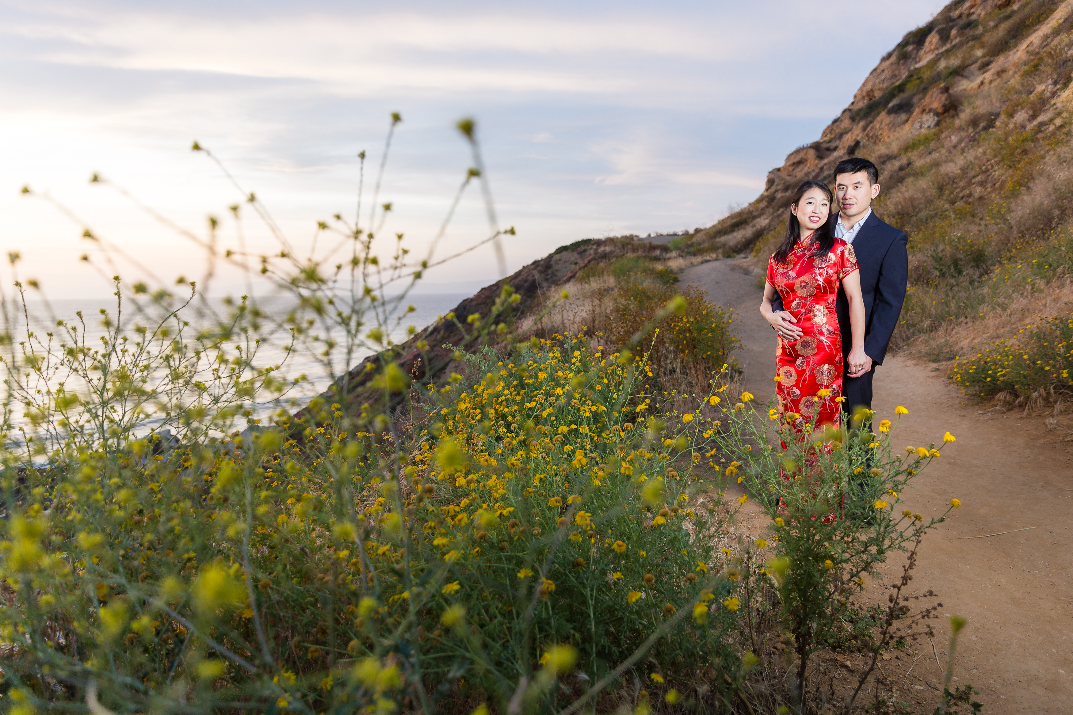 Engaged asian couple holding hands by yellow flowers on pathway in CA