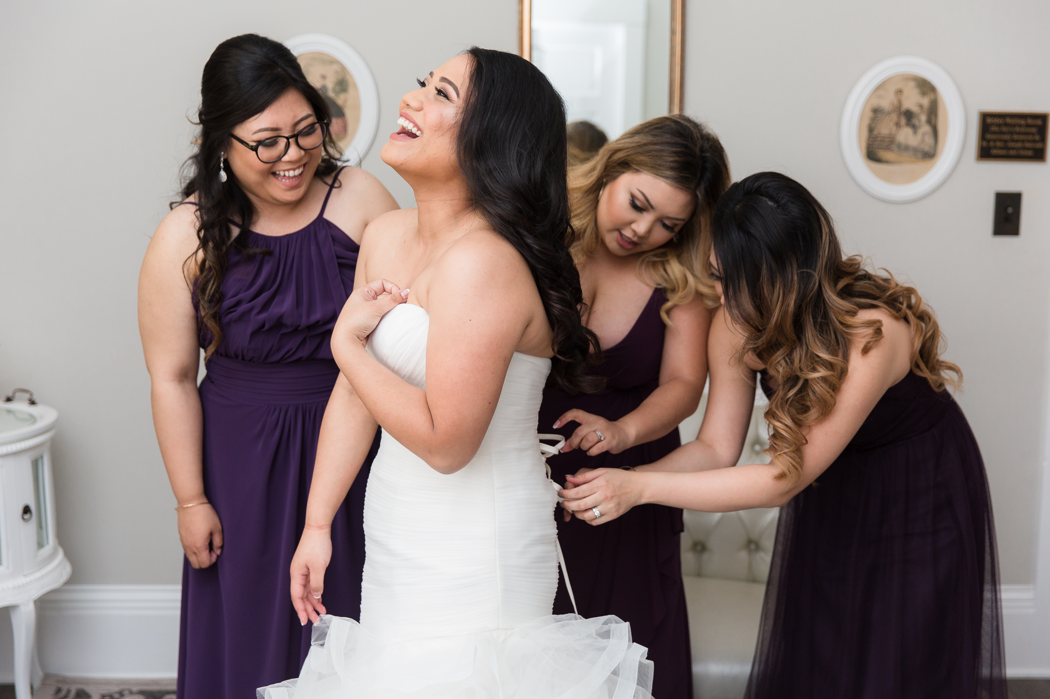 Bridesmaids lacing up laughing bride's wedding dress