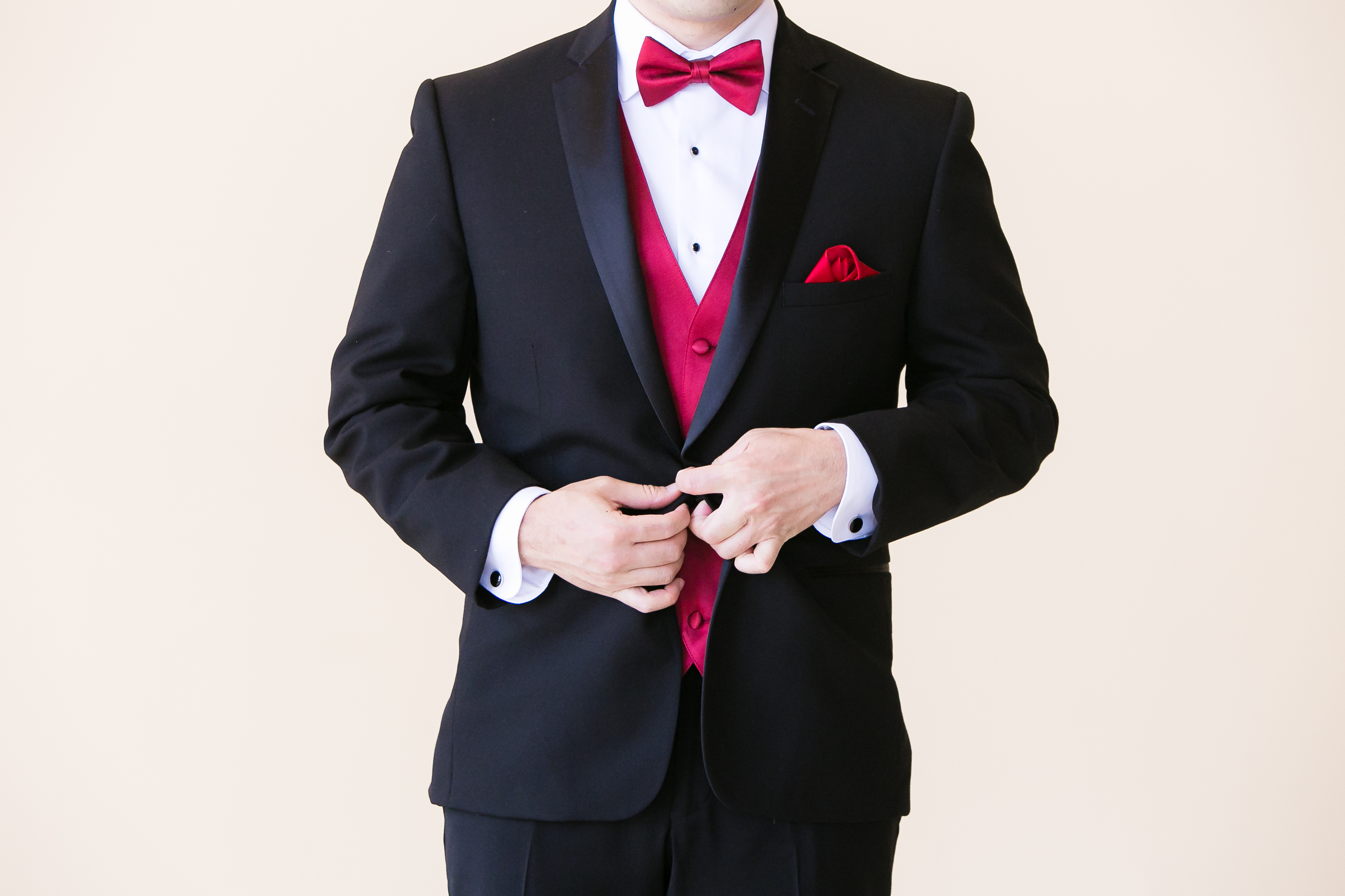 Groom buttoning tuxedo jacket with red vest and bow tie before Pacific Palms Resort Wedding