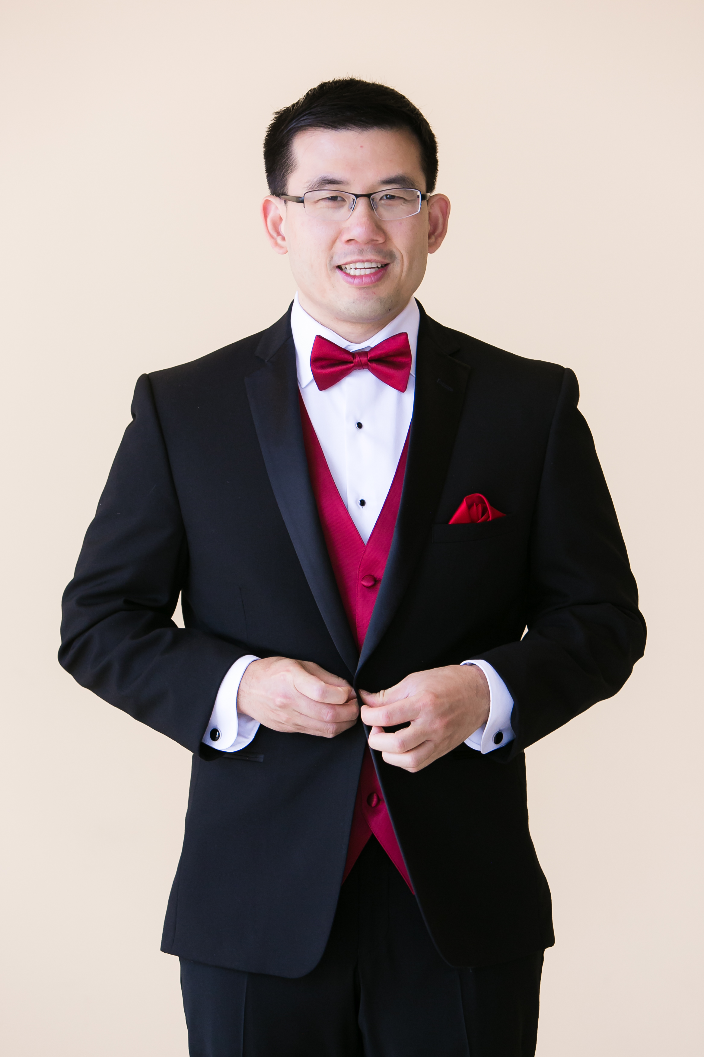 Groom getting into black tuxedo with red accents at Pacific Palms Resort Wedding
