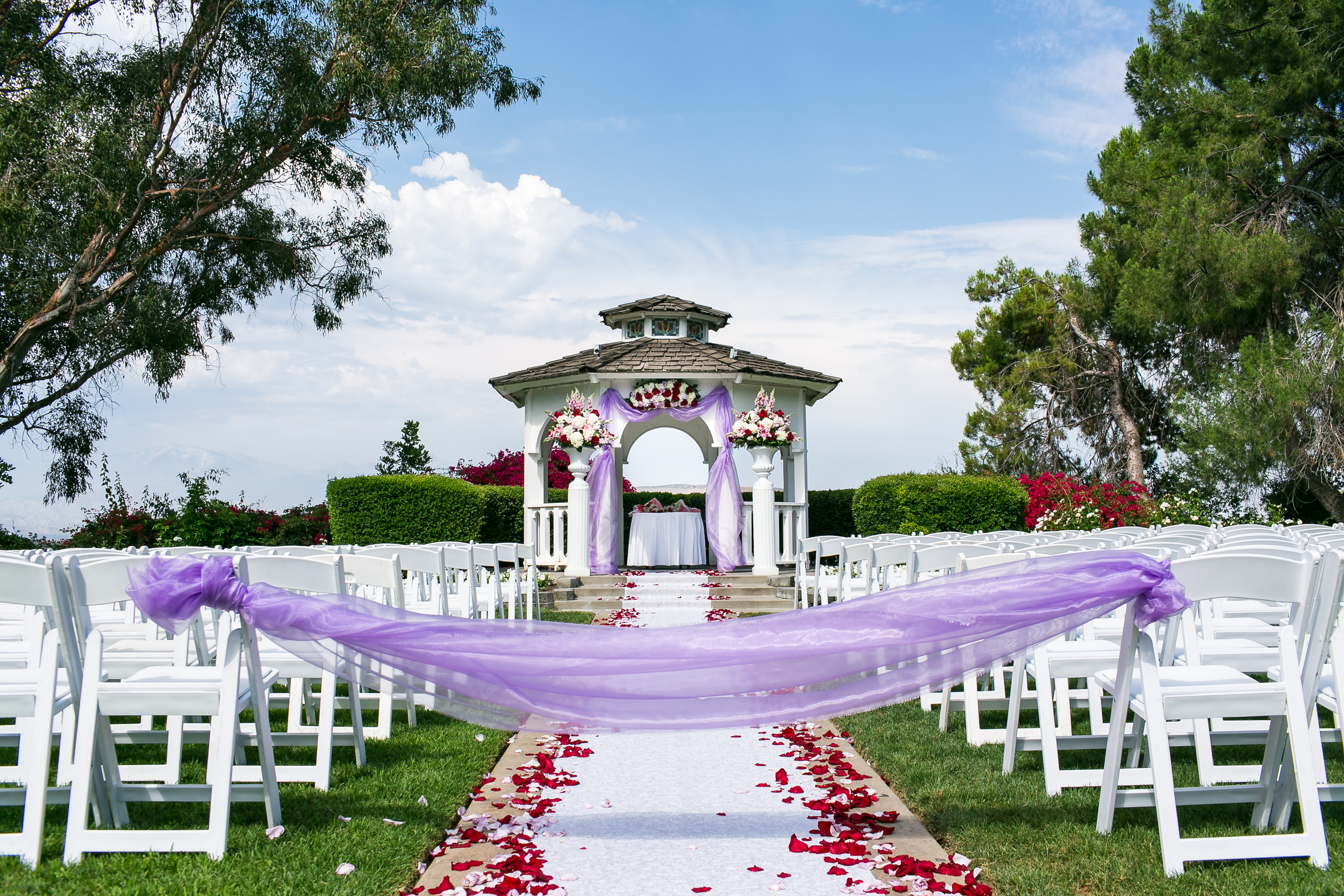 Ceremony aisle leading up to white gazebo with green trees and a blue sky