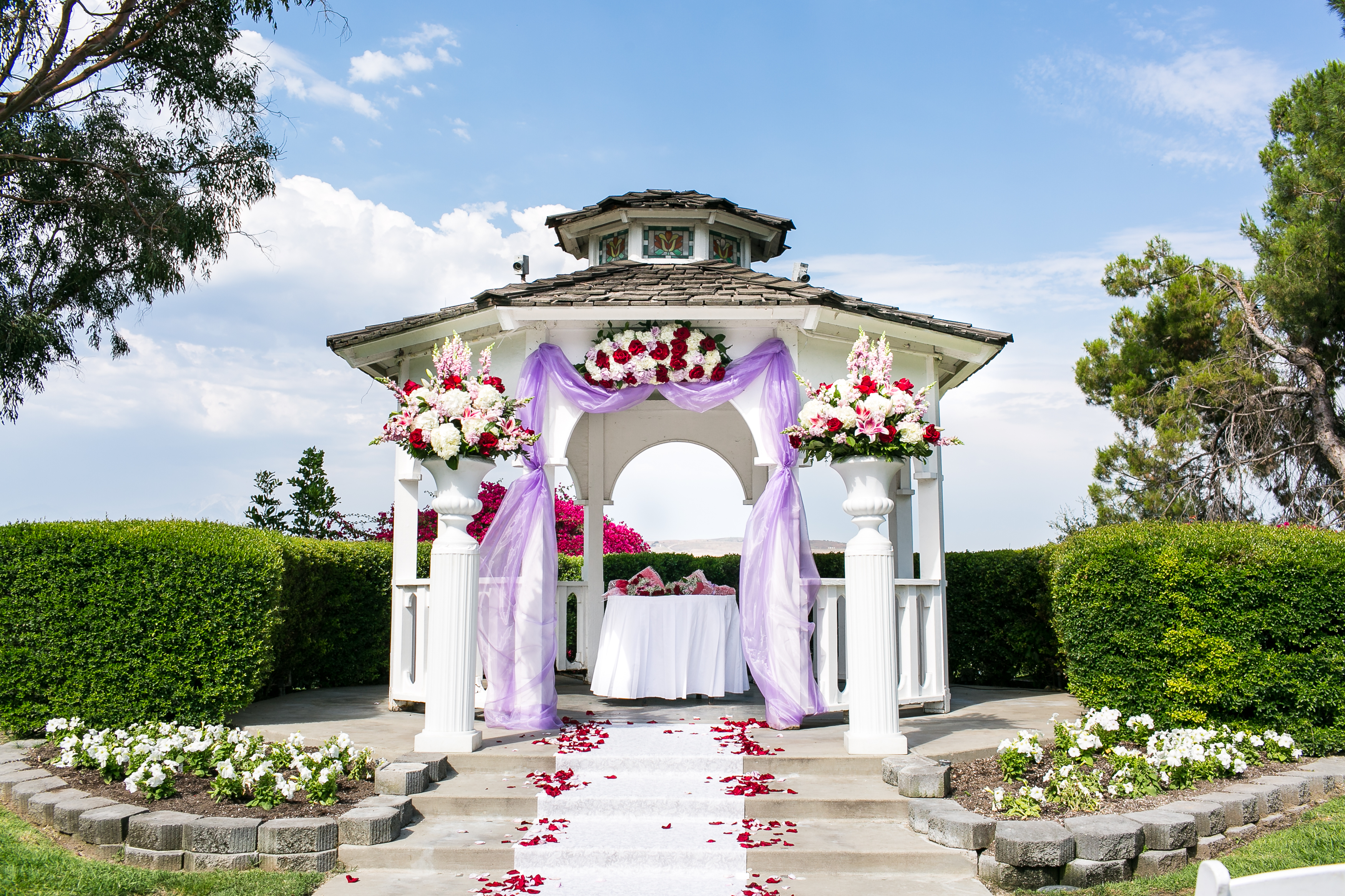 White gazebo with purple accent drapes covered in red and white flowers
