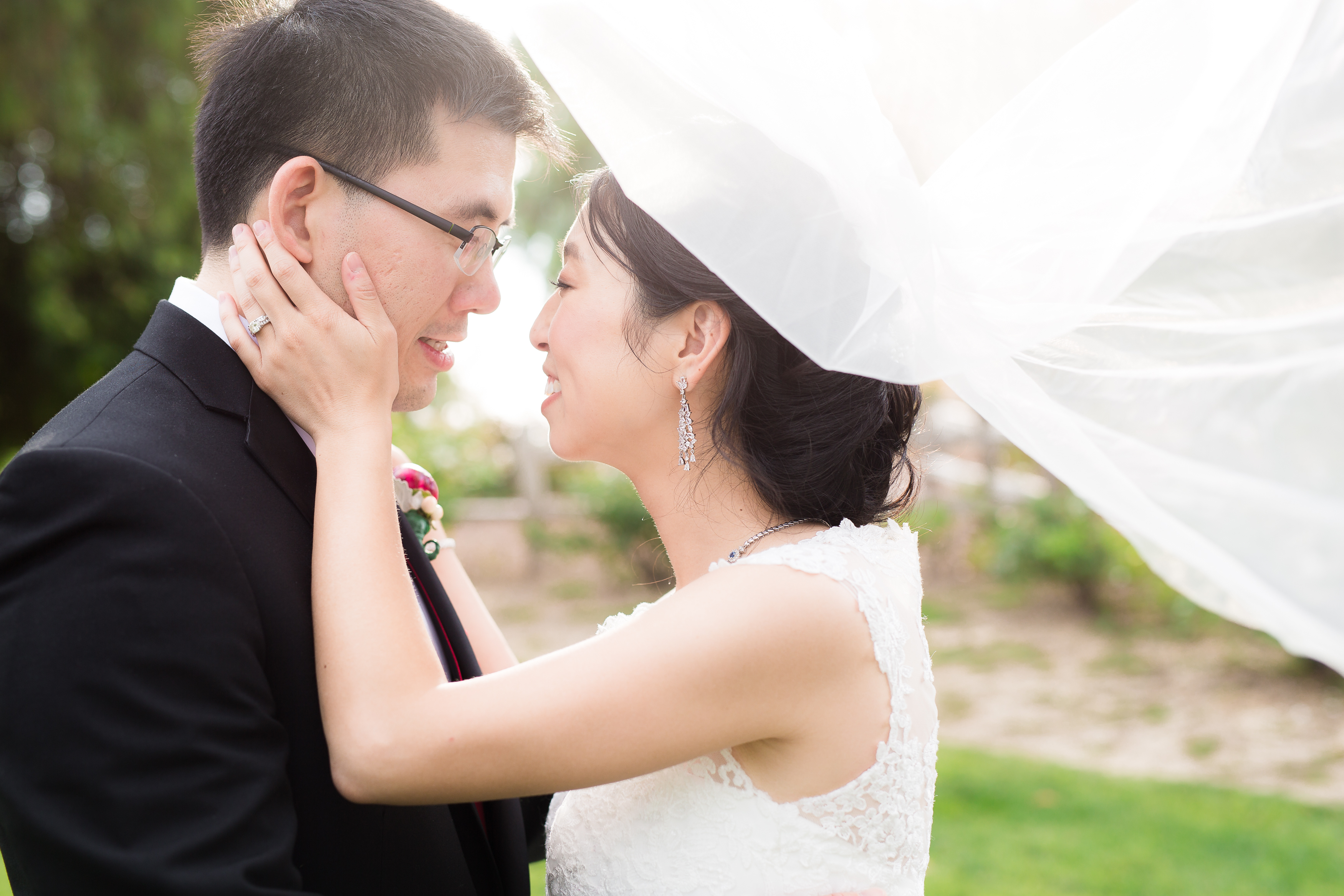 Bride cupping groom's face smiling with veil blowing in wind