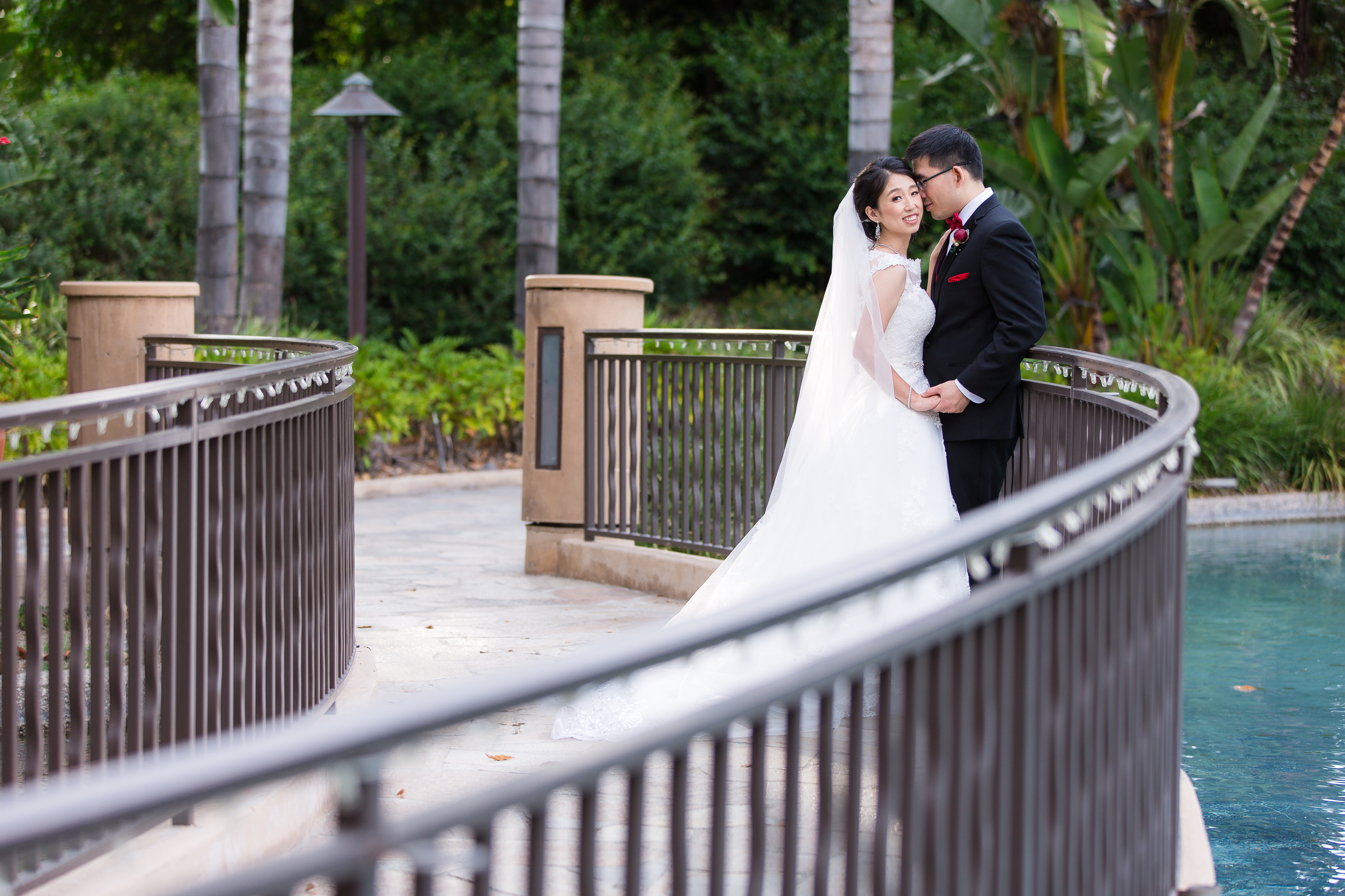 Groom snuggling into bride on bridge by water at Pacific Palms Resort Wedding