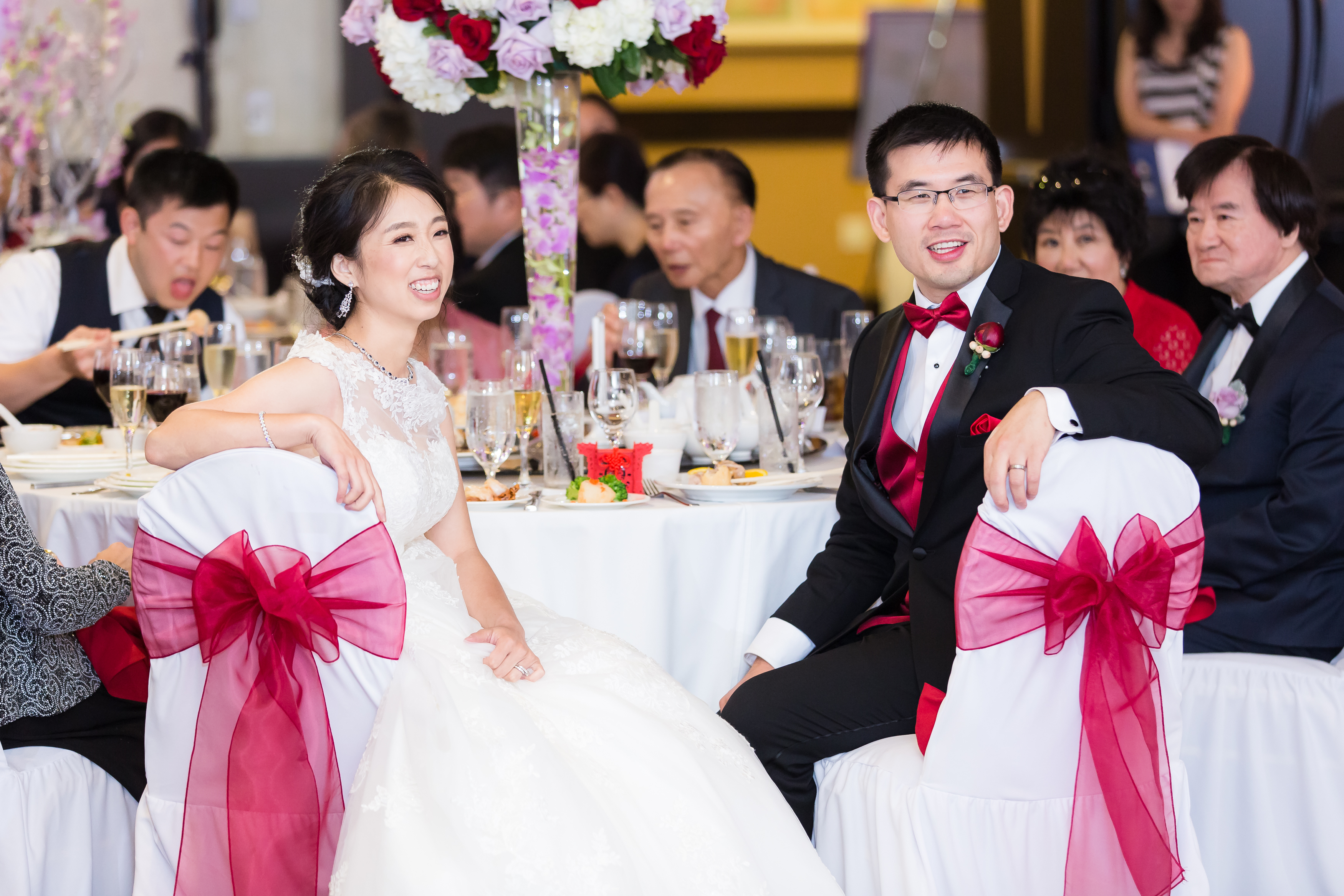 Wedding couple smiling and sitting in white chairs with red ribbons