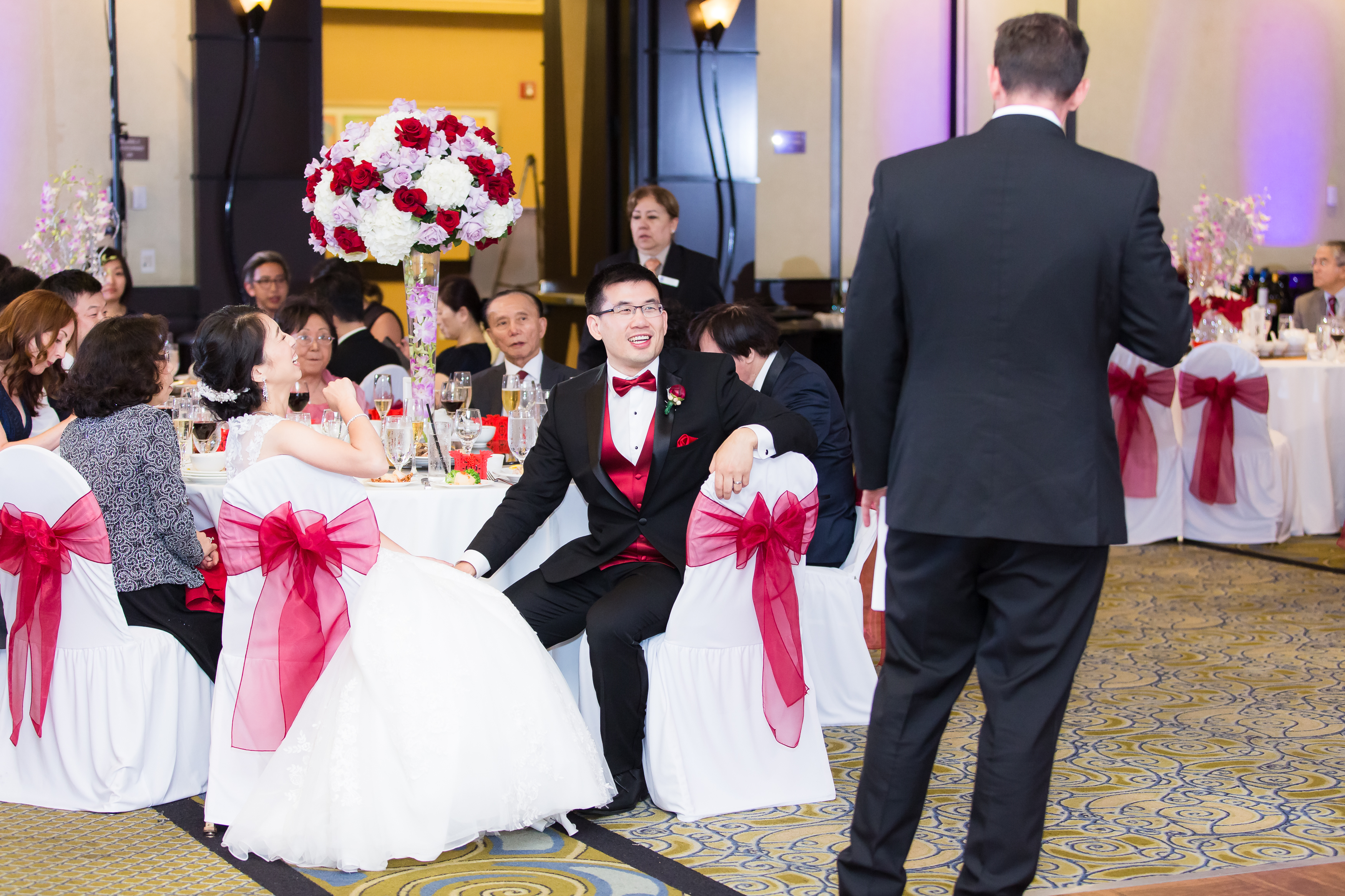 Wedding couple laughing at groomsman in banquet hall