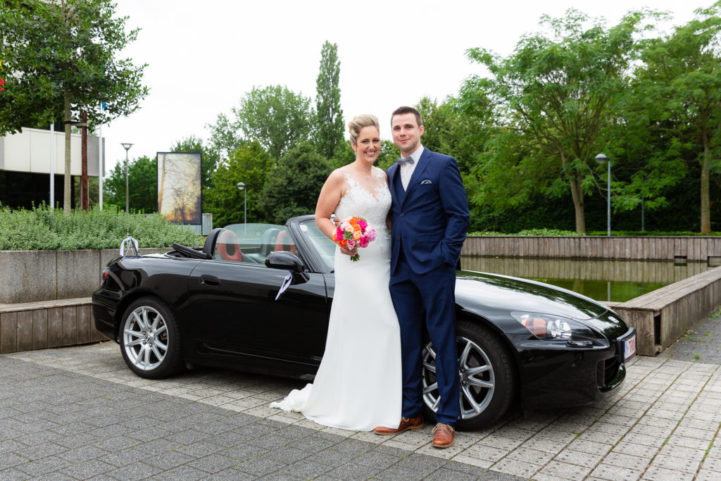 bride and groom standing in front of sports car