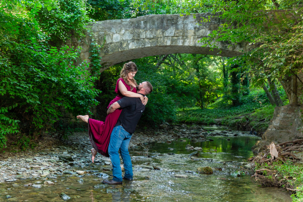 man lifting woman in creek under bridge for Dallas Photoshoot Location Prather Park Engagement Photo