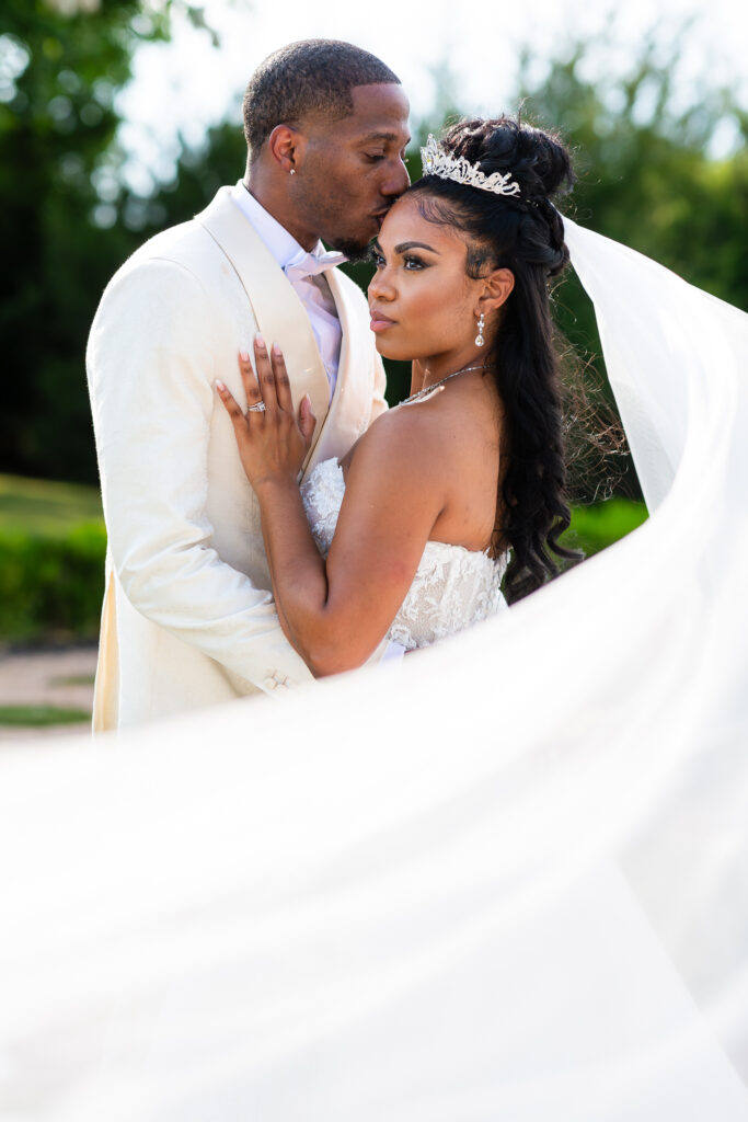 groom kissing bride's forehead with veil floating in the wind at knotting hill place by Stefani Ciotti Photography