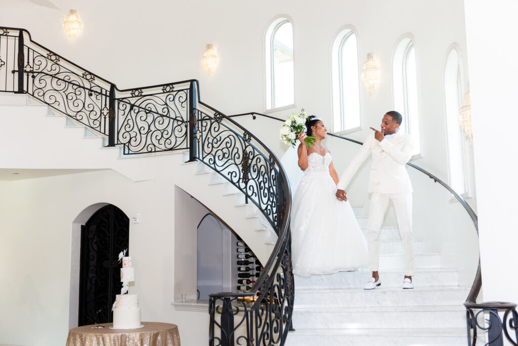 Bride and groom in all white walk down stairs during grand entrance into reception hall at knotting hill place