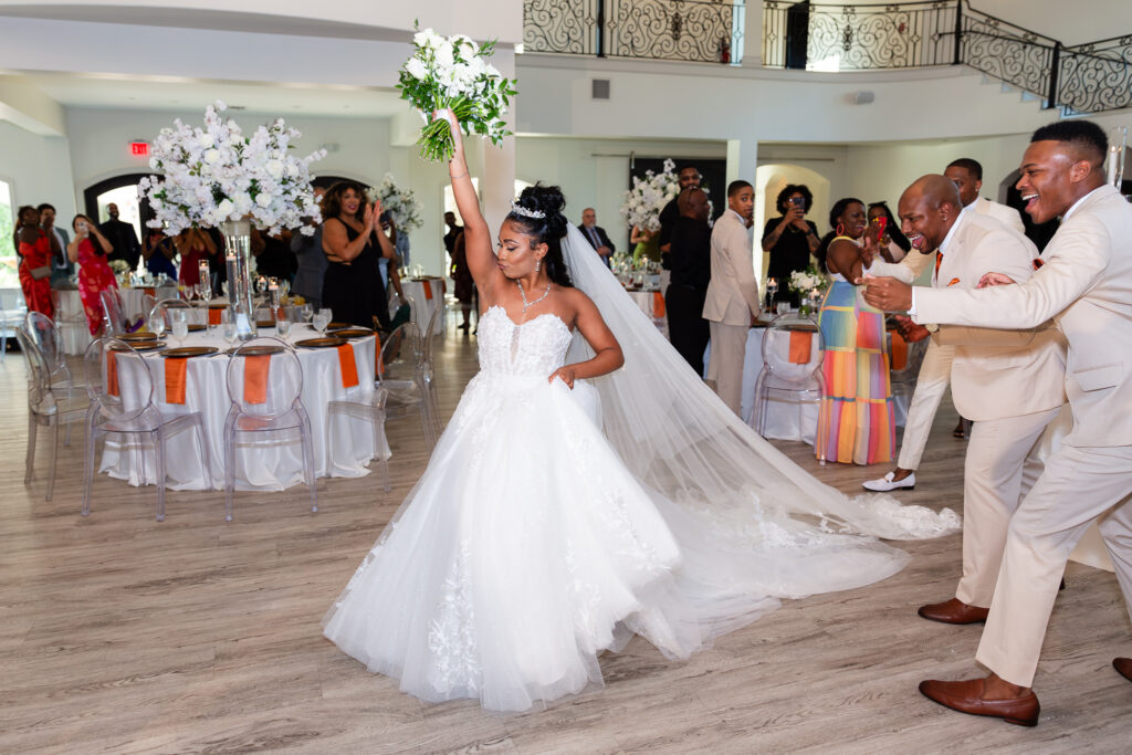 Bride cheers with white bouquet in the air while walking to dance floor during grand entrance into reception hall at knotting hill place