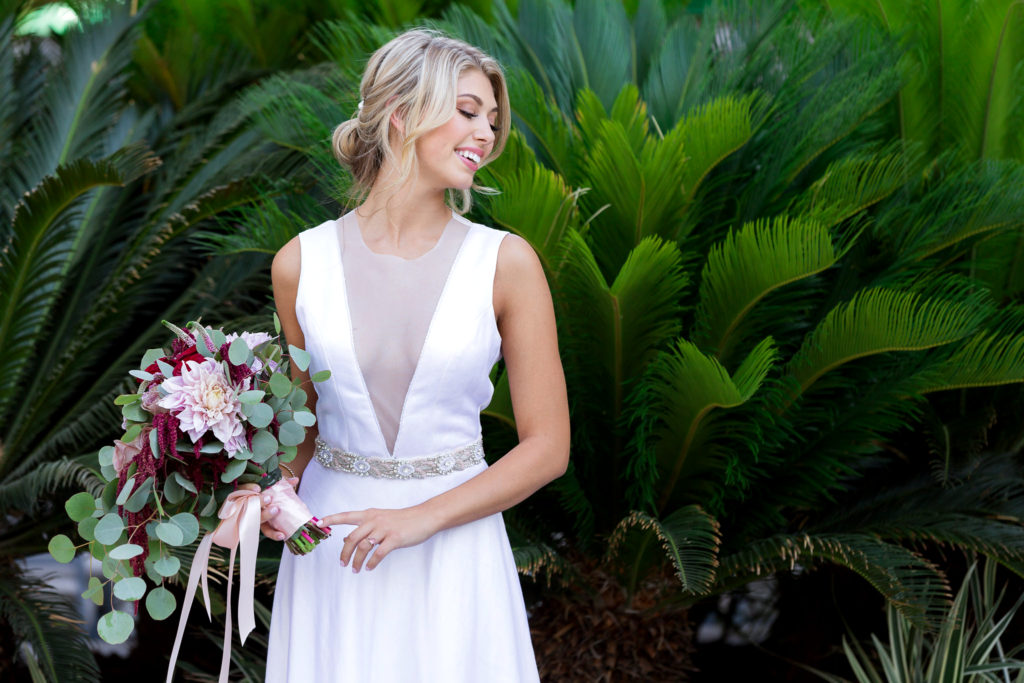 outdoor wedding in Dallas with bride in a satin wedding dress holding a floral bouquet and smiling over her shoulder photographed by Dallas wedding photographer