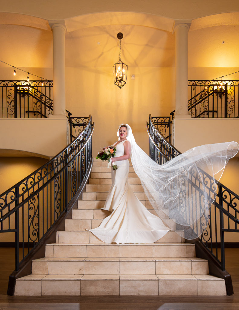 bride with floating veil standing on staircase in ballroom at chapel at ana villa in the colony tx