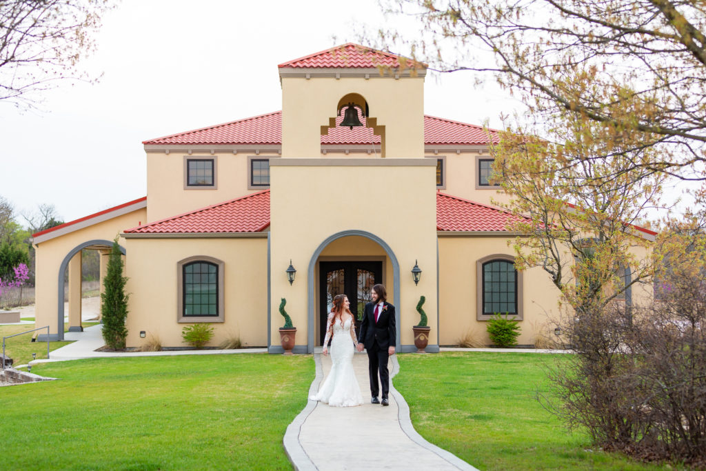 bride and groom holding hands and walking on the grounds of their Dallas wedding venue, Stoney Ridge Villa, with Dallas wedding photographers