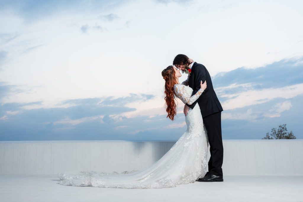 Bride and groom on rooftop on the Stoney Ridge Villa wedding venue with the sunset in the distance as the groom holding his bride and leans into her romantically