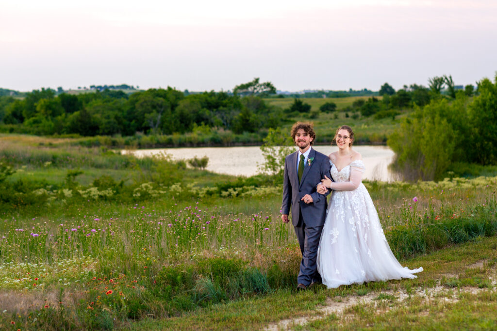 outdoor dallas wedding venue with bride and groom walking on the bank of a lake with lush brush surrounding them captured by Dallas wedding photographers 