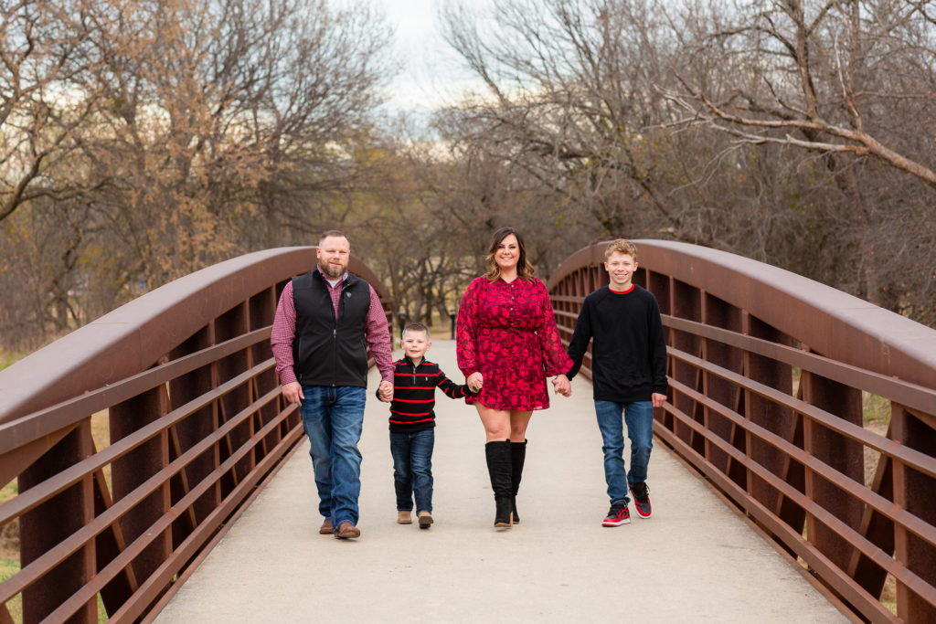 Family session with mom dad and two sons holding hands and walking across a bridge at keller pointe in keller texas