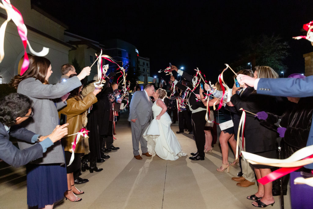 bride and groom kissing as they leave their wedding surrounded by streamers taken by Dallas wedding photographers