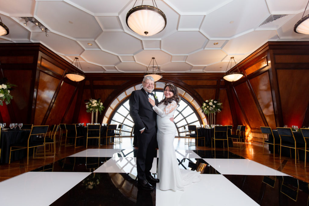 wedding portrait with bride and groom embracing in their reception space with a large window in the distance captured by Dallas wedding photographer at the Hotel Crescent Court