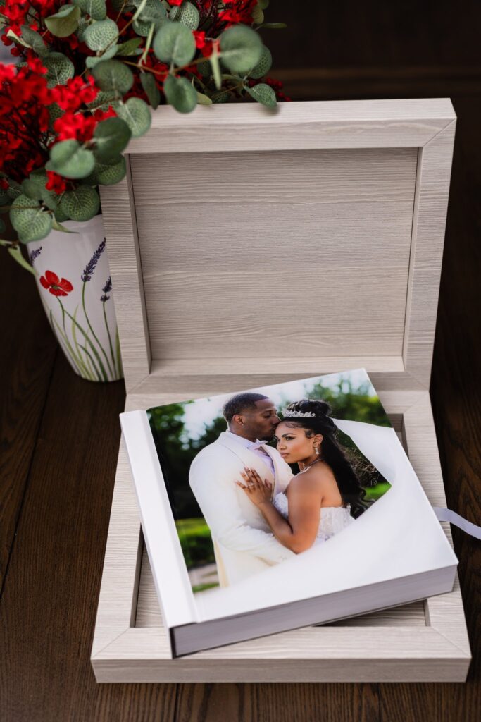 italian, handcrafted wedding album with acrylic photo cover of groom kissing bride on the temple sits in a light colored wood heirloom box