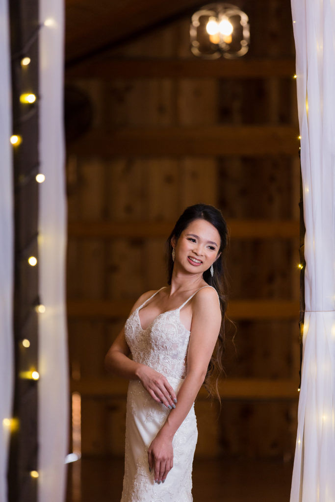 Dallas wedding photographer photographs bride in a lace wedding dress inside of a barn decorated with twinkle light and white drapes