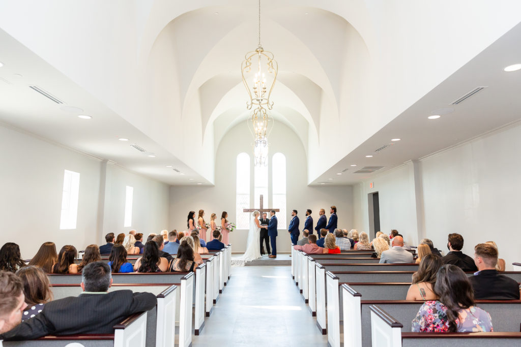 Bride and groom say their wedding vows as Dallas wedding photographers capture wide angle shot of the ceremony and guests in a white minimalistic venue in Dallas TX