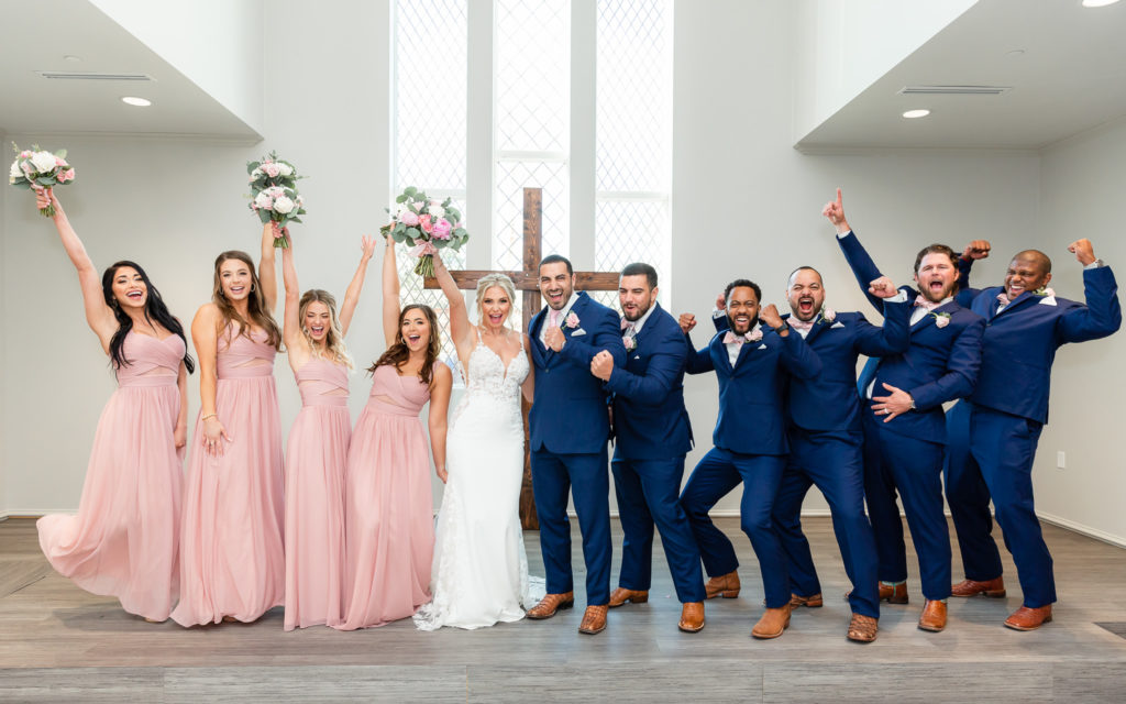 bridal party surrounding the bride and groom at the Dallas wedding venue with their arms in the air in celebration captured by Dallas wedding photographer 