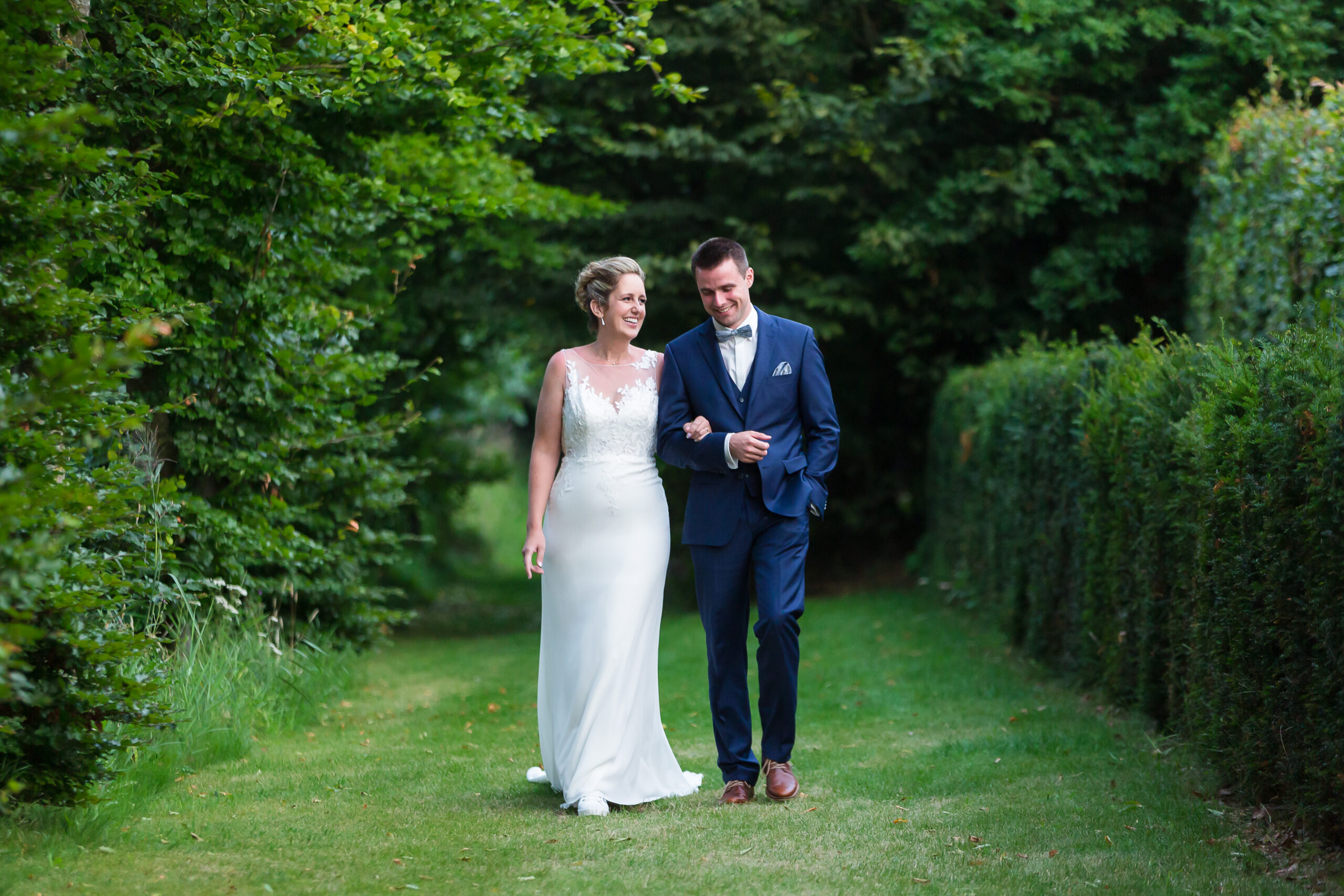 outdoor Dallas wedding day with bride and groom locking arms and walking through a lush green garden talking and smiling with one another captured by Dallas wedding photographers