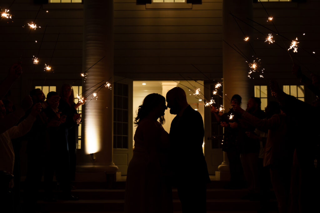 grand exit with bride adn groom standing outside of their wedding venue in the dark surrounded by sparklers captured by dallas wedding photographer