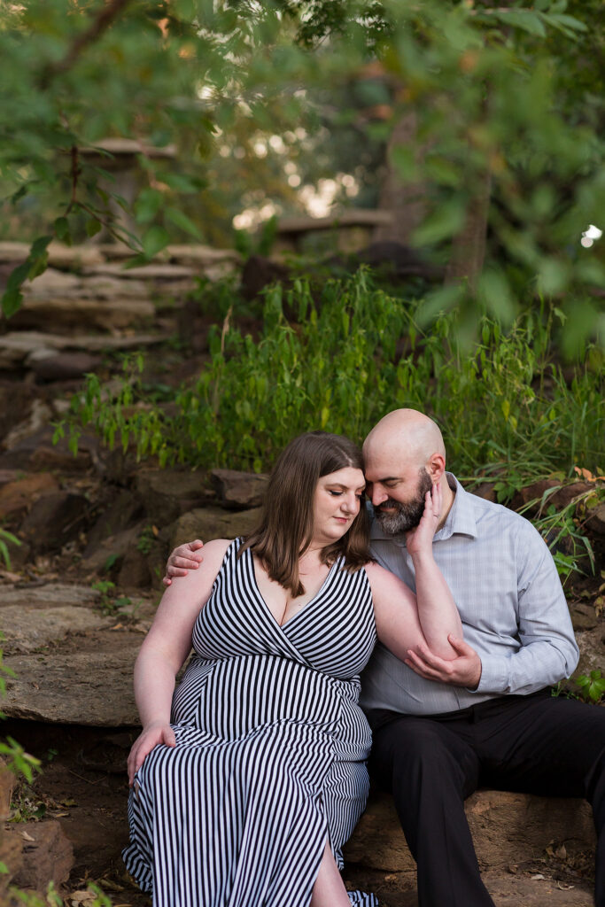 Engaged couple sitting forehead to forehead on a rock stair pathway with foliage surrounding them