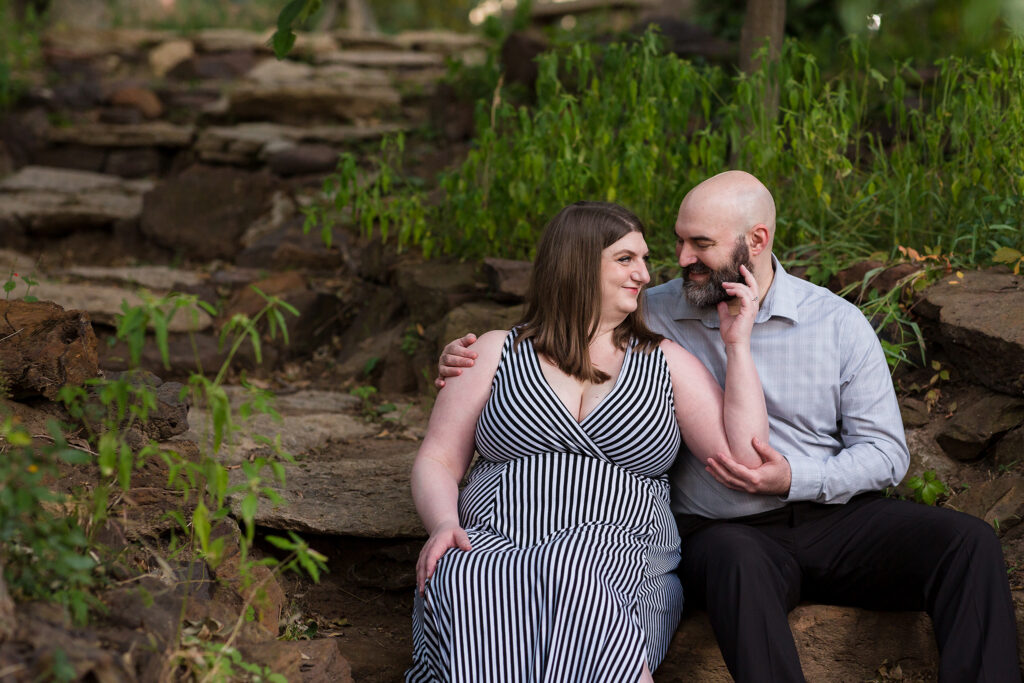 Engaged couple sitting together intimately on a rock stair pathway with foliage