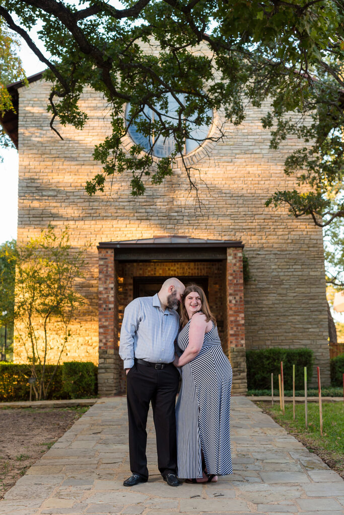 Dallas wedding photographer photographs Dallas engagement pictures with man and woman in grey outfits nuzzling into each other and standing in front of an old building at Texas Woman's University