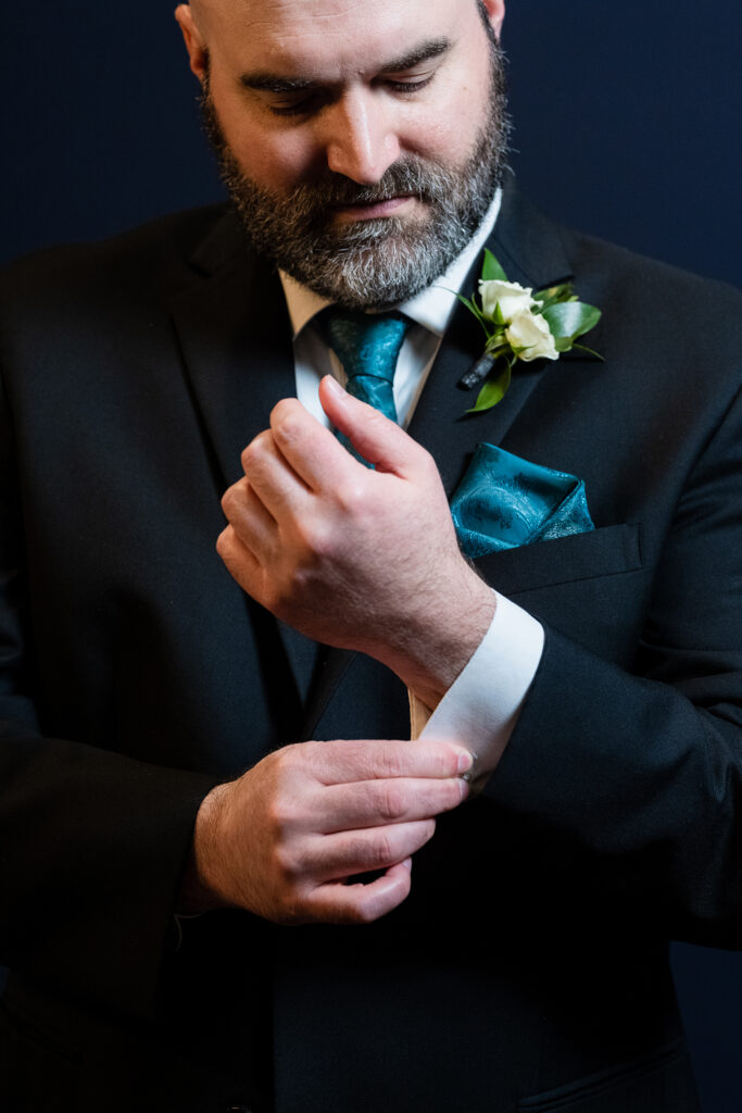 Groom adjusts cufflinks in black suit and teal tie