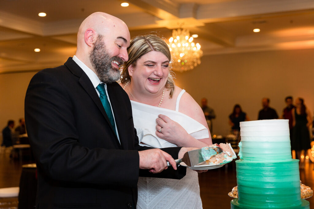Bride and groom smile and laugh while cutting white and green wedding cake during wedding reception at Milestone venue in denton texas