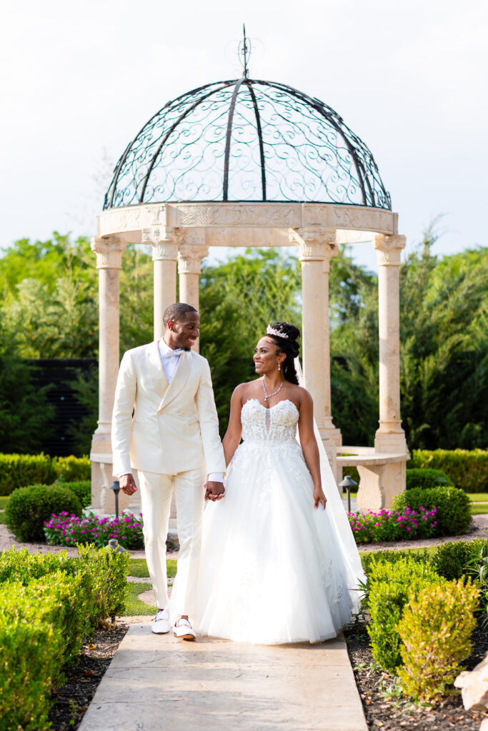Dallas wedding photographers capture bride and groom holding hands looking at one another with gazebo behind them